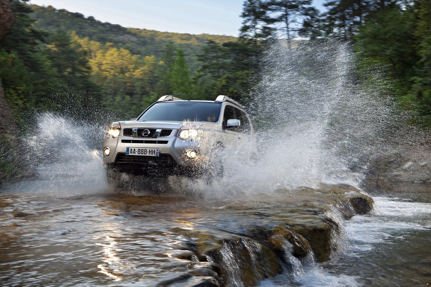 SUV fährt durch einen flachen Fluss, spritzt Wasser auf, umgeben von üppigem, grünem Wald. Dynamische Offroad-Szene.