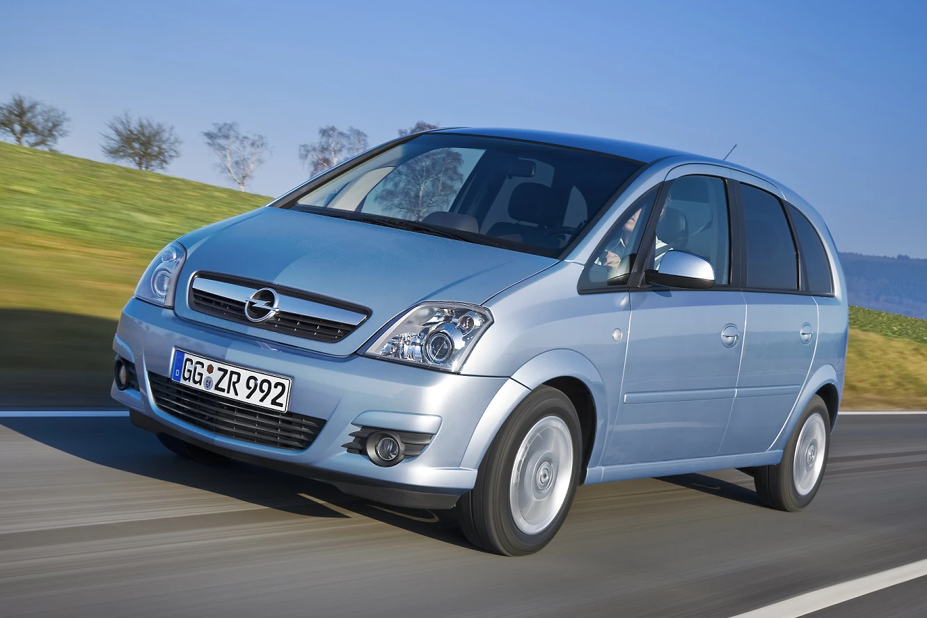 Silberner Opel Zafira fährt auf einer Landstraße, Bäume und Wiesen im Hintergrund. Fahrzeugfront und Seite sind sichtbar.