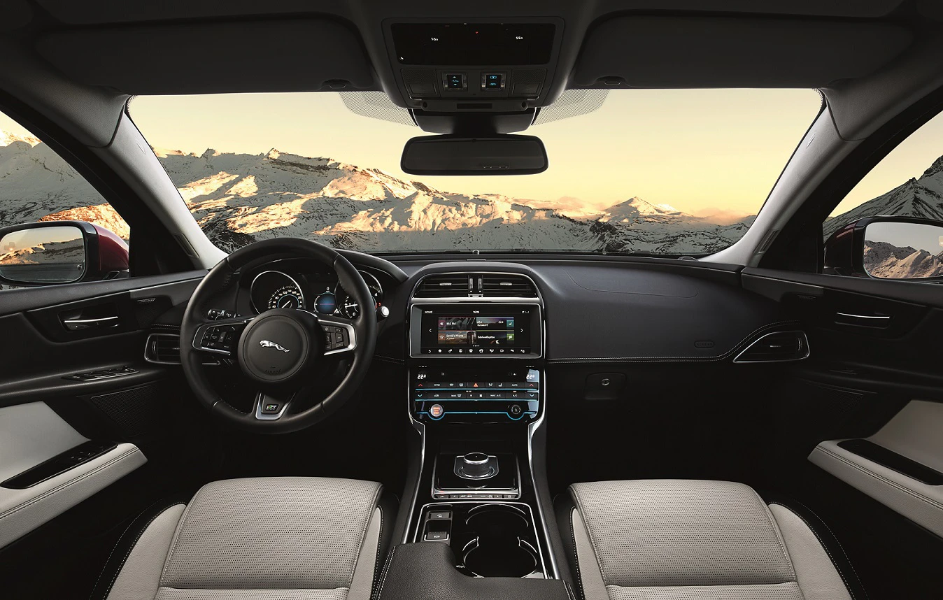 Innenansicht eines Autos mit Blick aus der Windschutzscheibe auf schneebedeckte Berge im Hintergrund, modernes Armaturenbrett und Lenkrad.