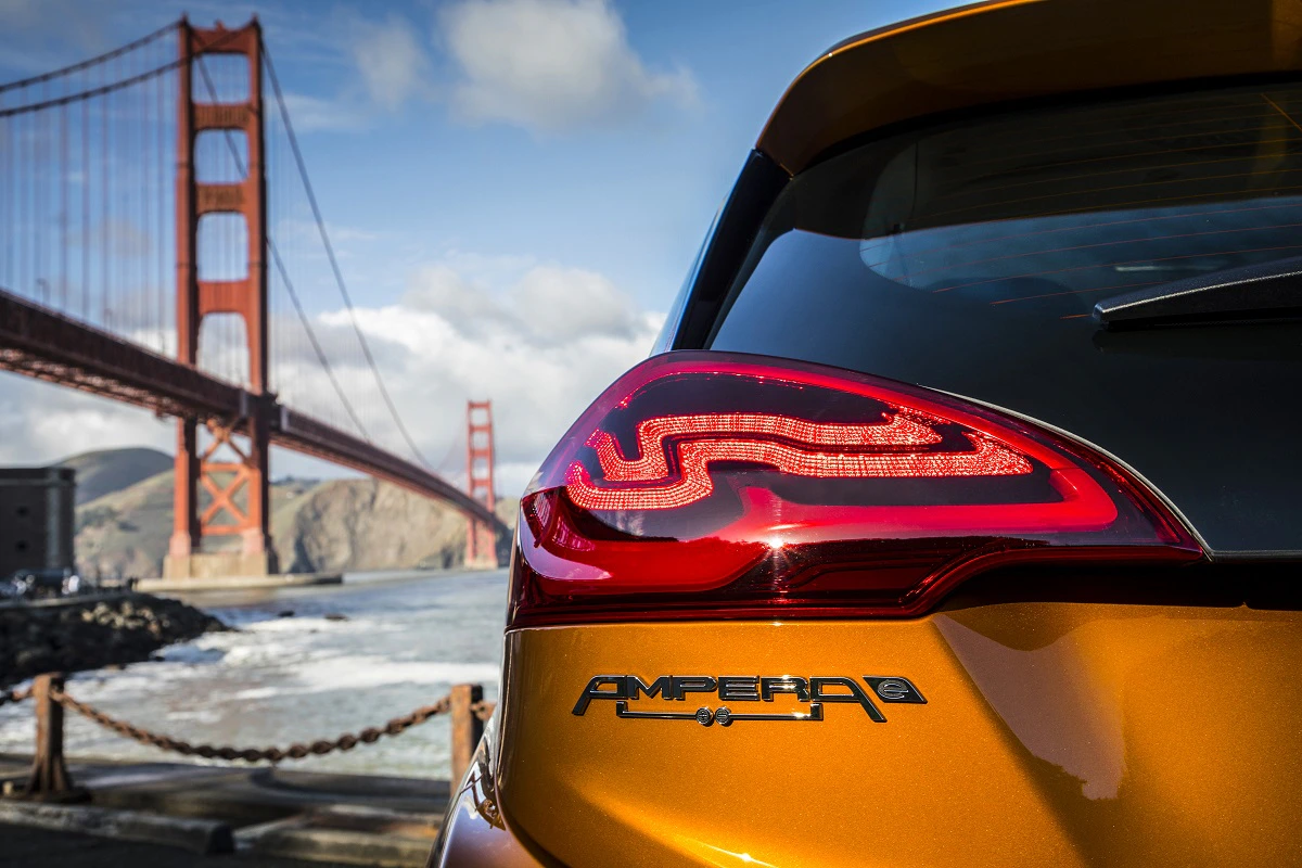 Nahaufnahme eines goldenen Autos mit beleuchtetem Rücklicht. Im Hintergrund die Golden Gate Bridge vor blauem Himmel und Wasser.