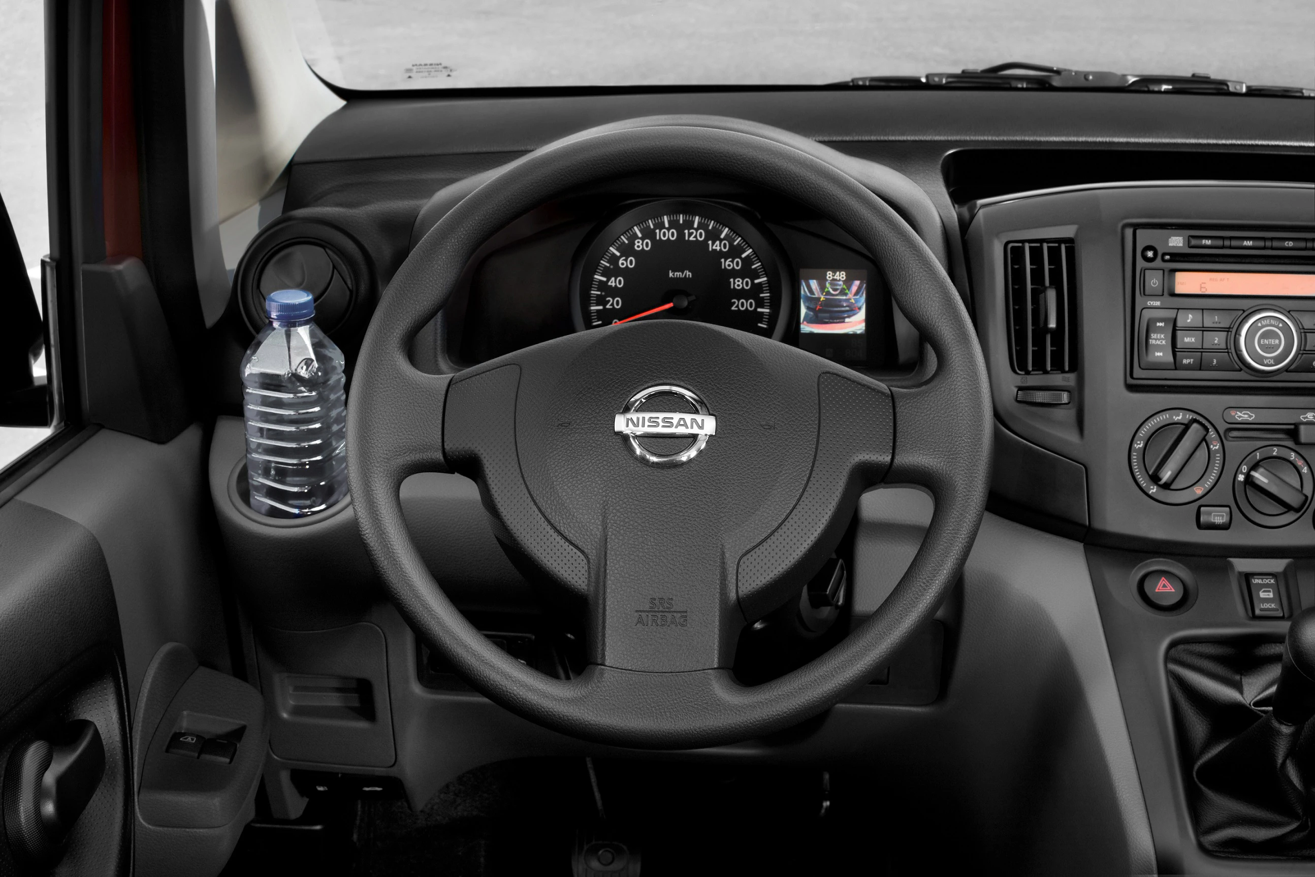 Innenraum eines Autos mit einem Nissan-Lenkrad, Tacho und einer Wasserflasche links im Getränkehalter. Rechts das Autoradio und Bedienelemente.