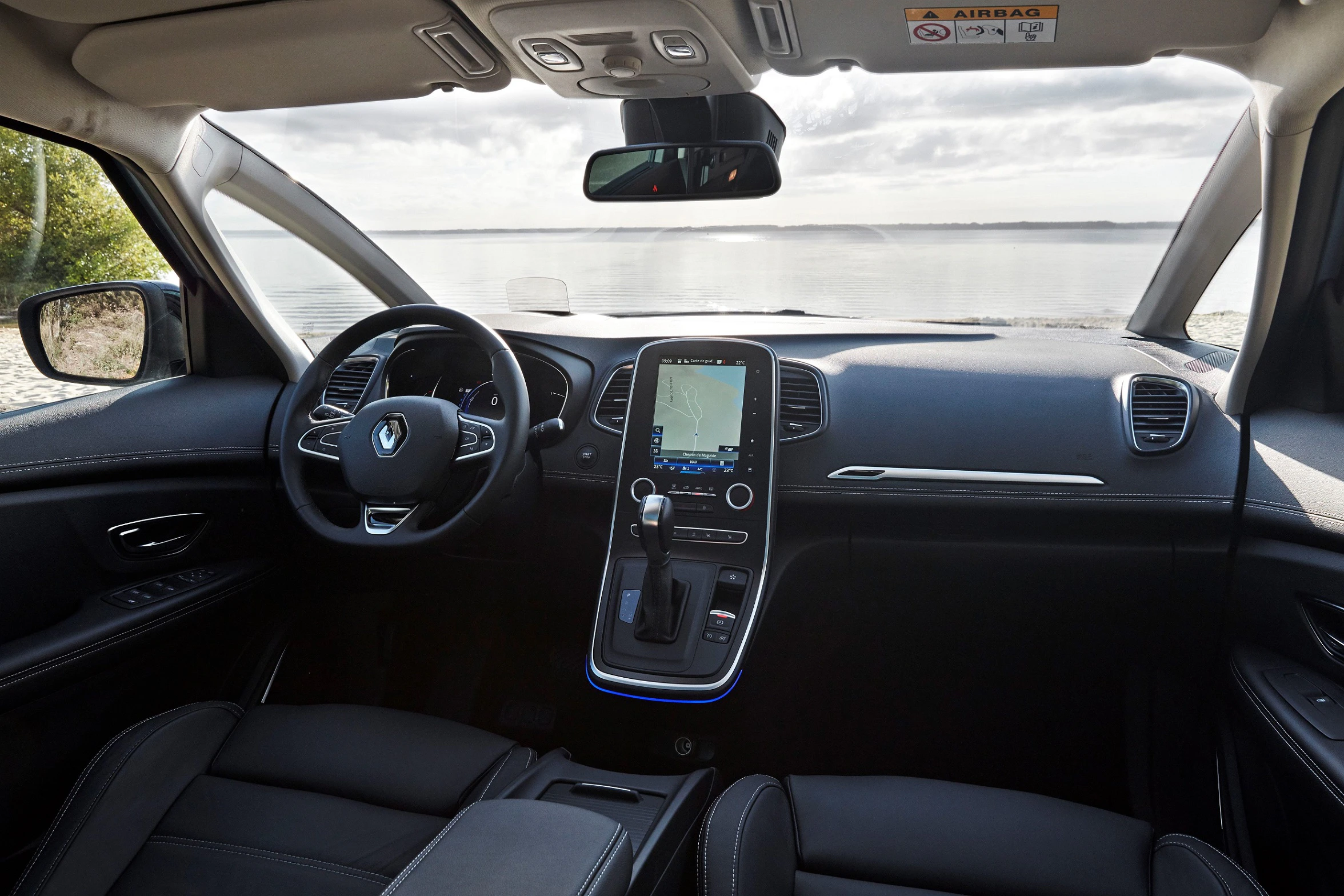 Innenraum eines Autos mit Blick aufs Wasser durchs Fenster. Modernes Armaturenbrett mit Touchscreen und schwarzer Polsterung.