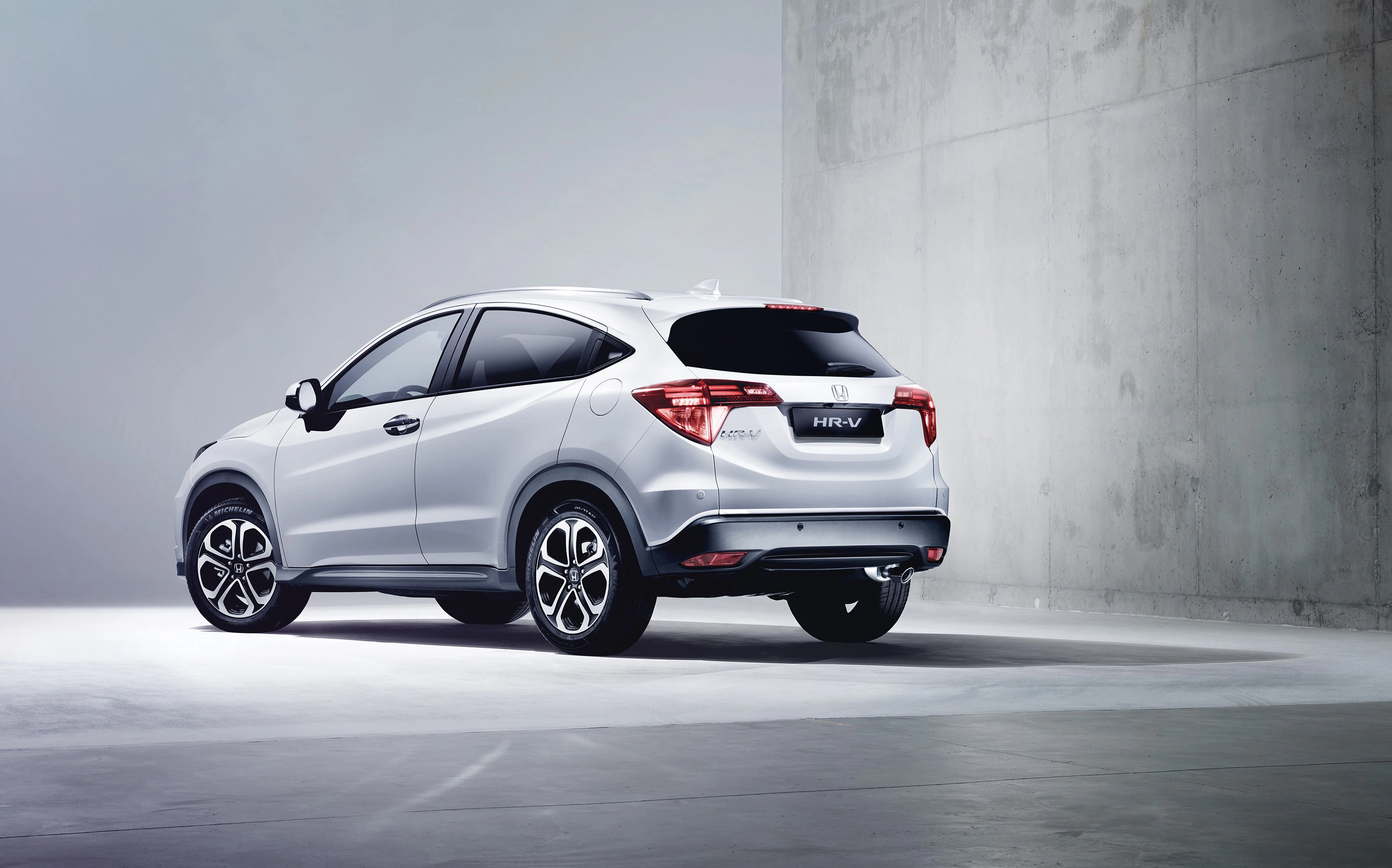 Silberner SUV parkt in minimalistischem Raum mit Betonwand, Heckansicht sichtbar. Elegant und modern.