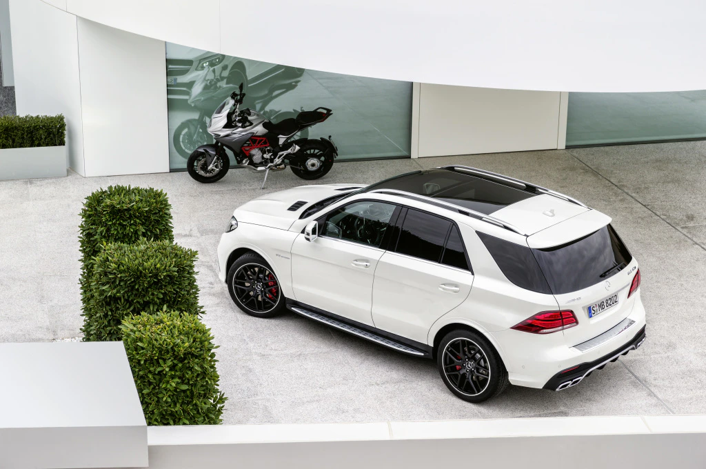 Weißer SUV und Motorrad vor einem modernen Gebäude mit Glasfront, umgeben von grünen Büschen und Beton.