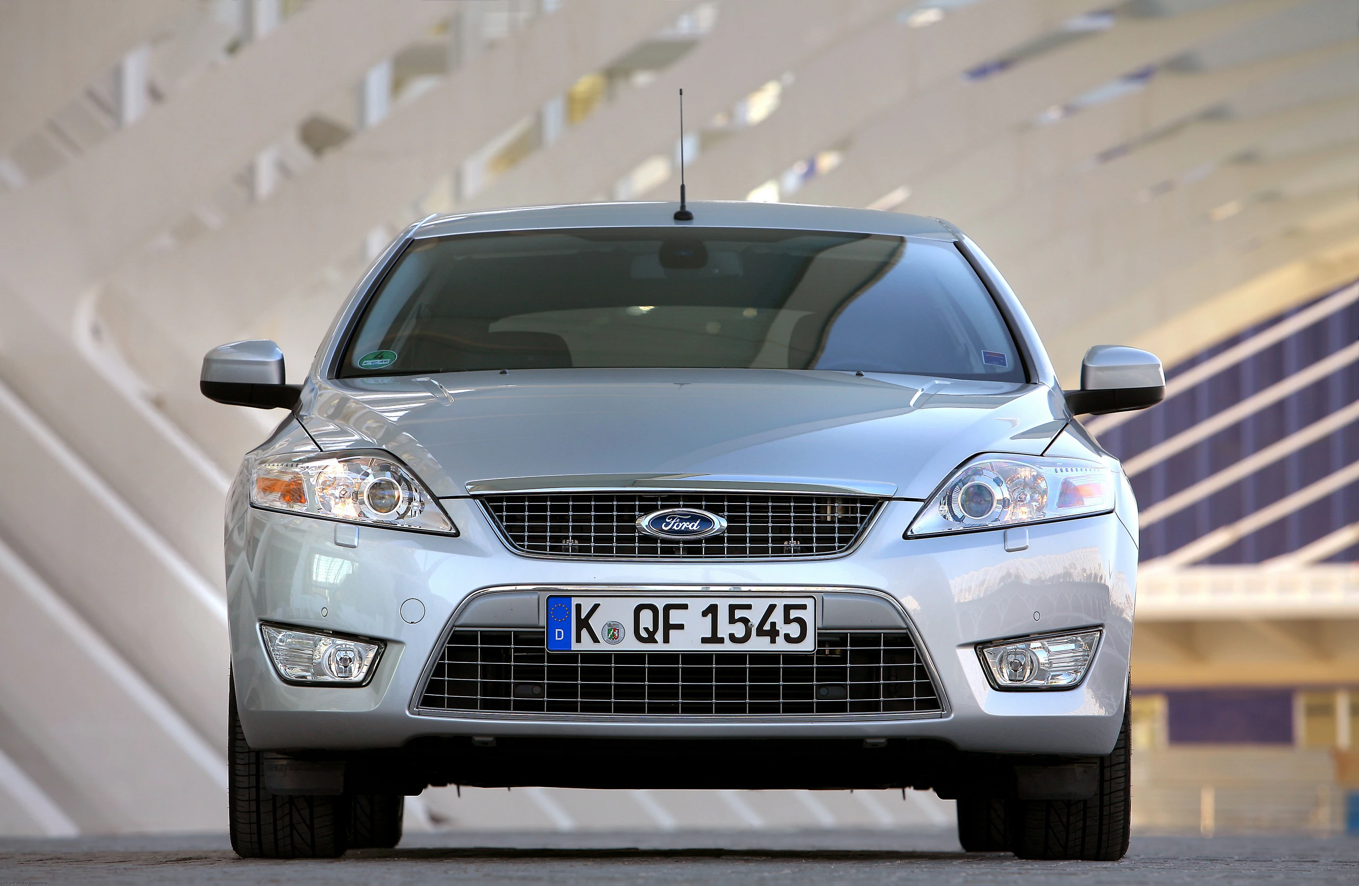 Silberner Ford Mondeo steht frontal auf einer Straße, modernes Hintergrunddesign.
