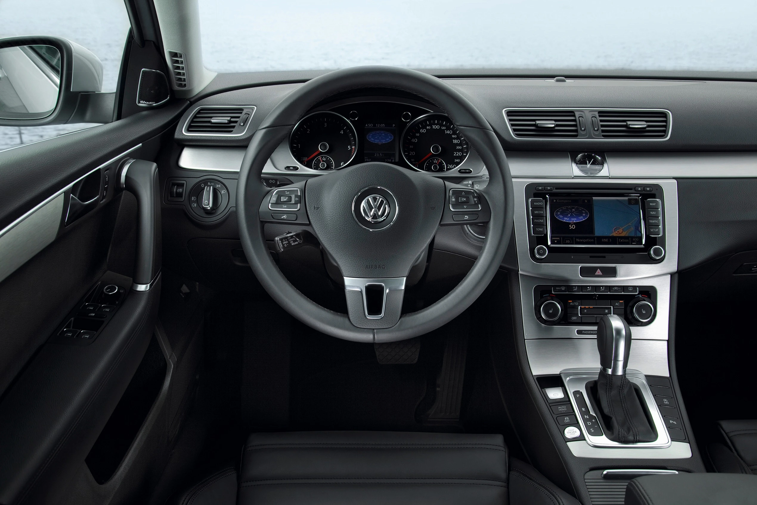 Innenraum eines VW-Autos mit Lenkrad, Tacho, Touchscreen und Automatikgetriebe. Modernes, elegantes Design mit schwarzer Lederausstattung.