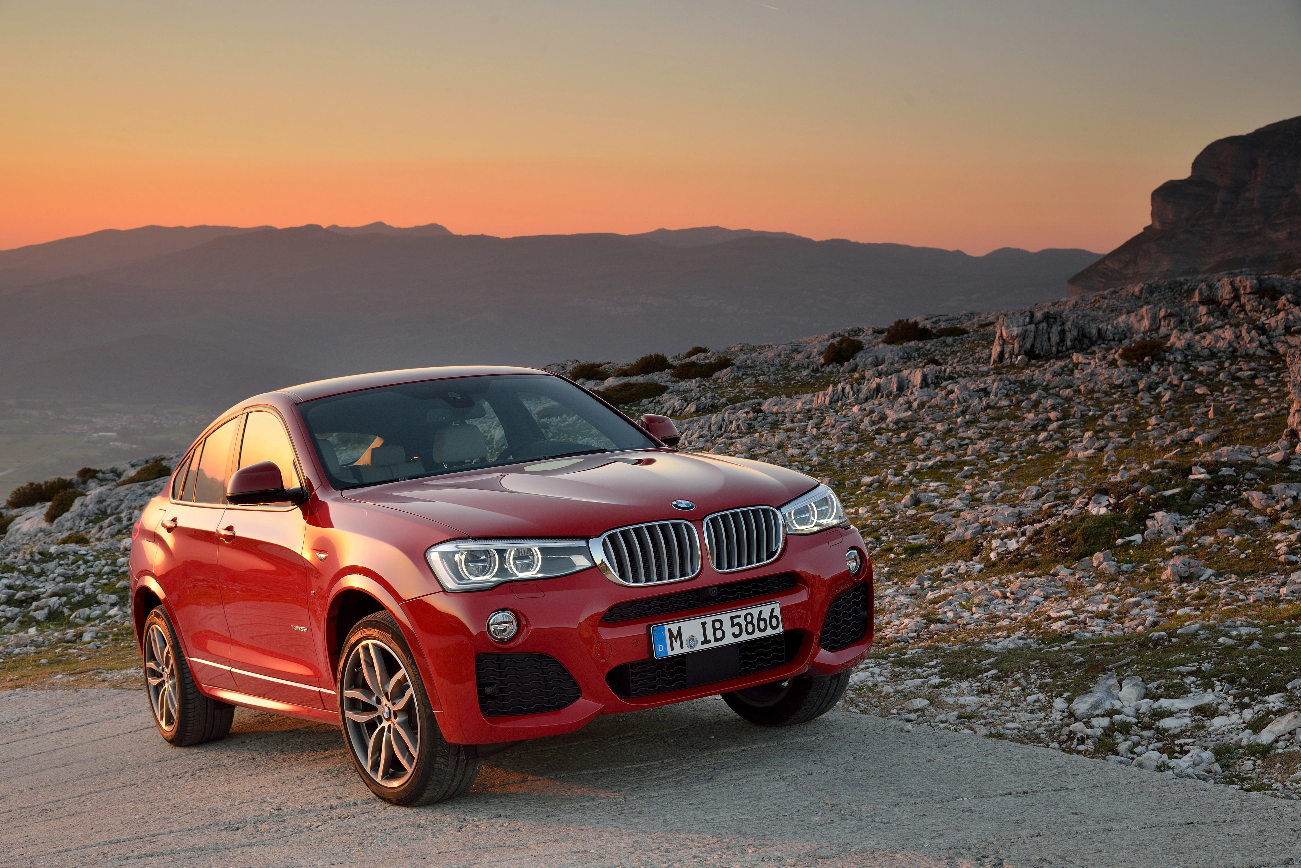 Roter SUV auf einer Kiesstraße bei Sonnenuntergang in bergiger Landschaft.