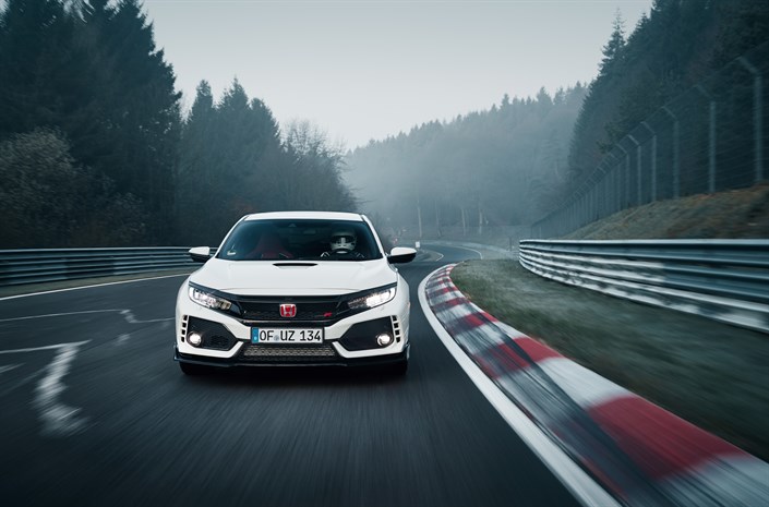 Weißer Honda Civic Type R fährt schnell auf nebliger, kurvenreicher Rennstrecke durch bewaldete Landschaft.