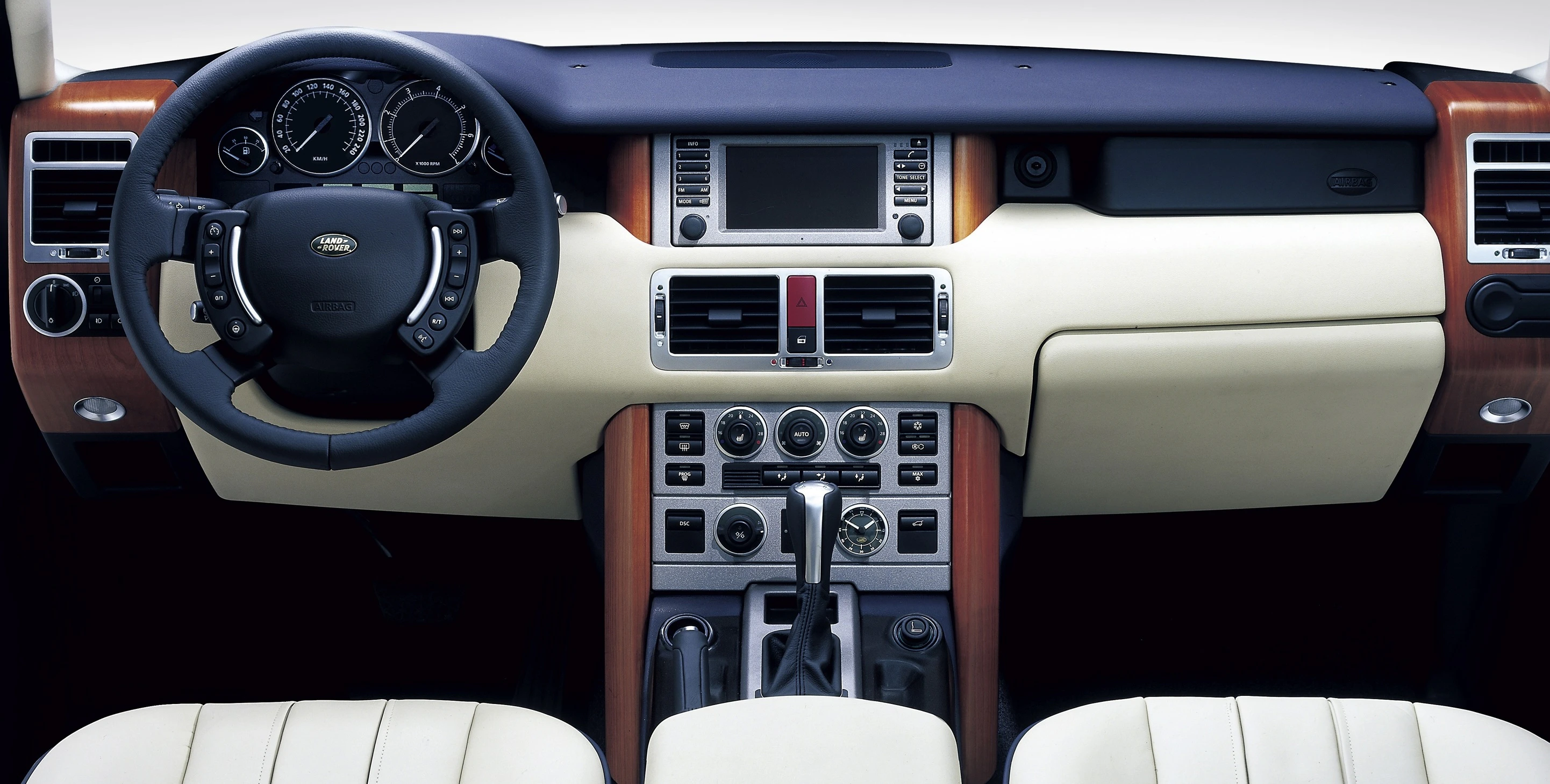 Innenansicht eines Autos mit luxuriösem Armaturenbrett aus Holz und Leder, Lenkrad links, viele Tasten und ein Bildschirm in der Mitte.