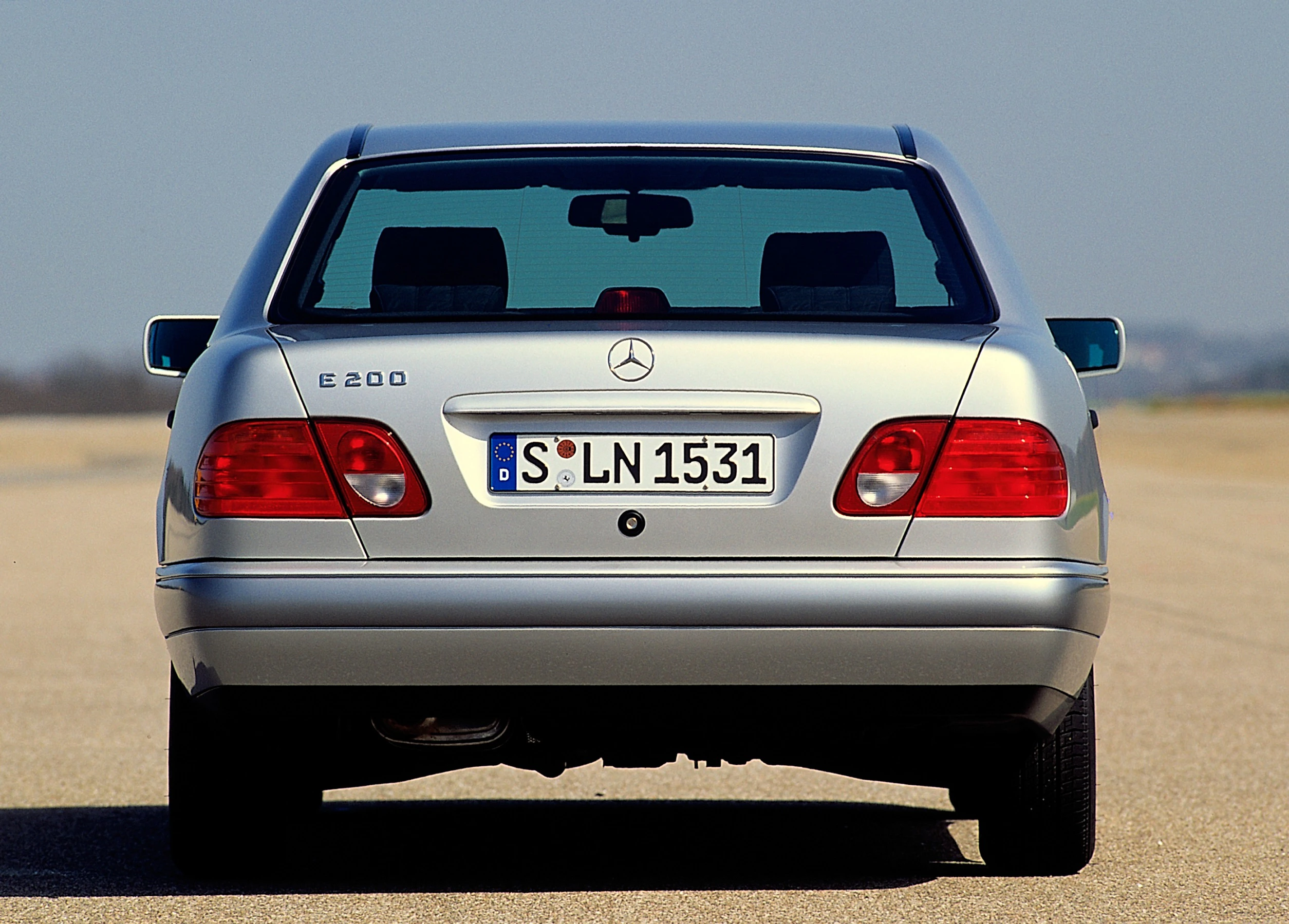 Silberner Mercedes-Benz E200 von hinten auf einer Straße, mit deutschem Nummernschild. Himmel und Horizont im Hintergrund.
