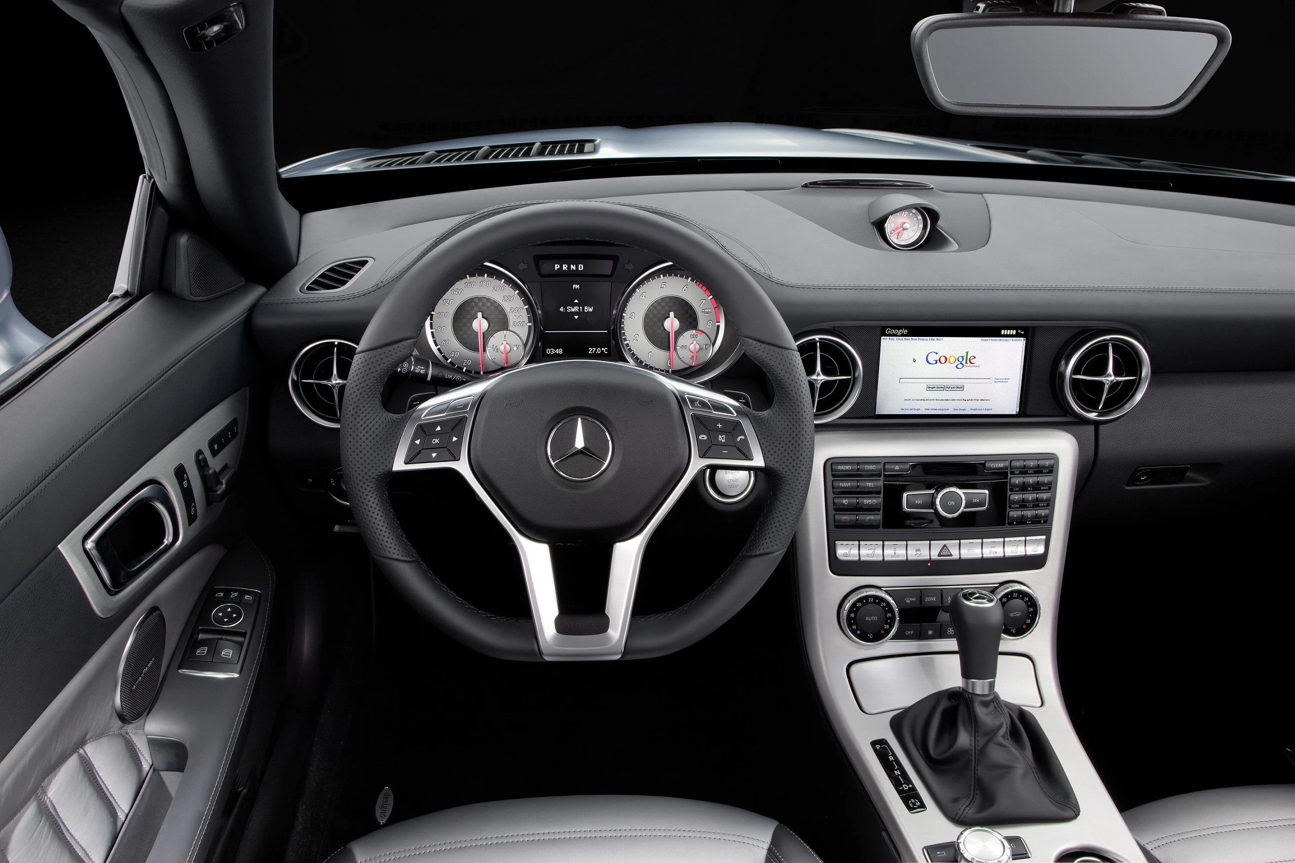 Innenraum eines Mercedes-Autos mit Lenkrad, Armaturenbrett und Mittelkonsole. Sicht auf Tacho, Navigationssystem und Belüftung.
