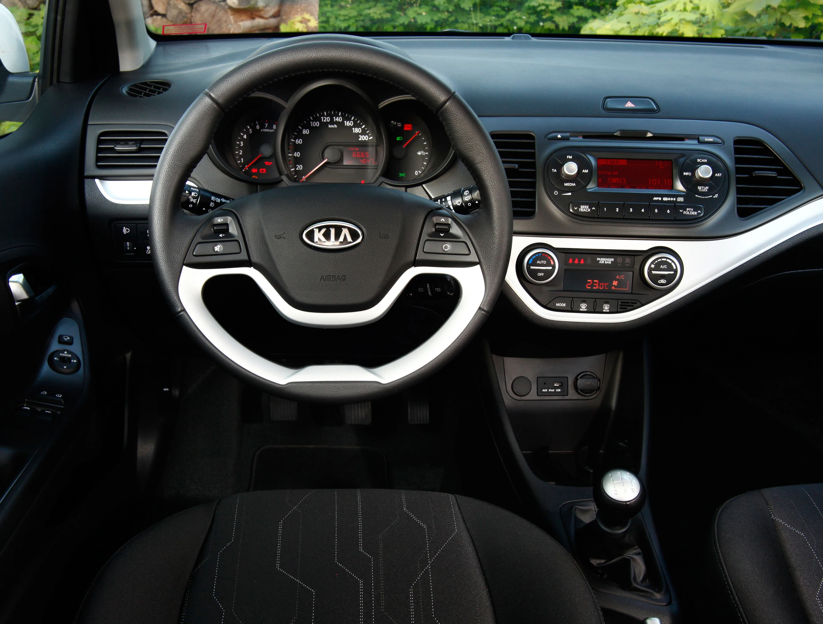 Innenraum eines Autos mit stilvollem Lenkrad, Tachometer und Mittelkonsole, die das Radio und Klimasteuerung zeigt. Markenlogo in der Mitte.