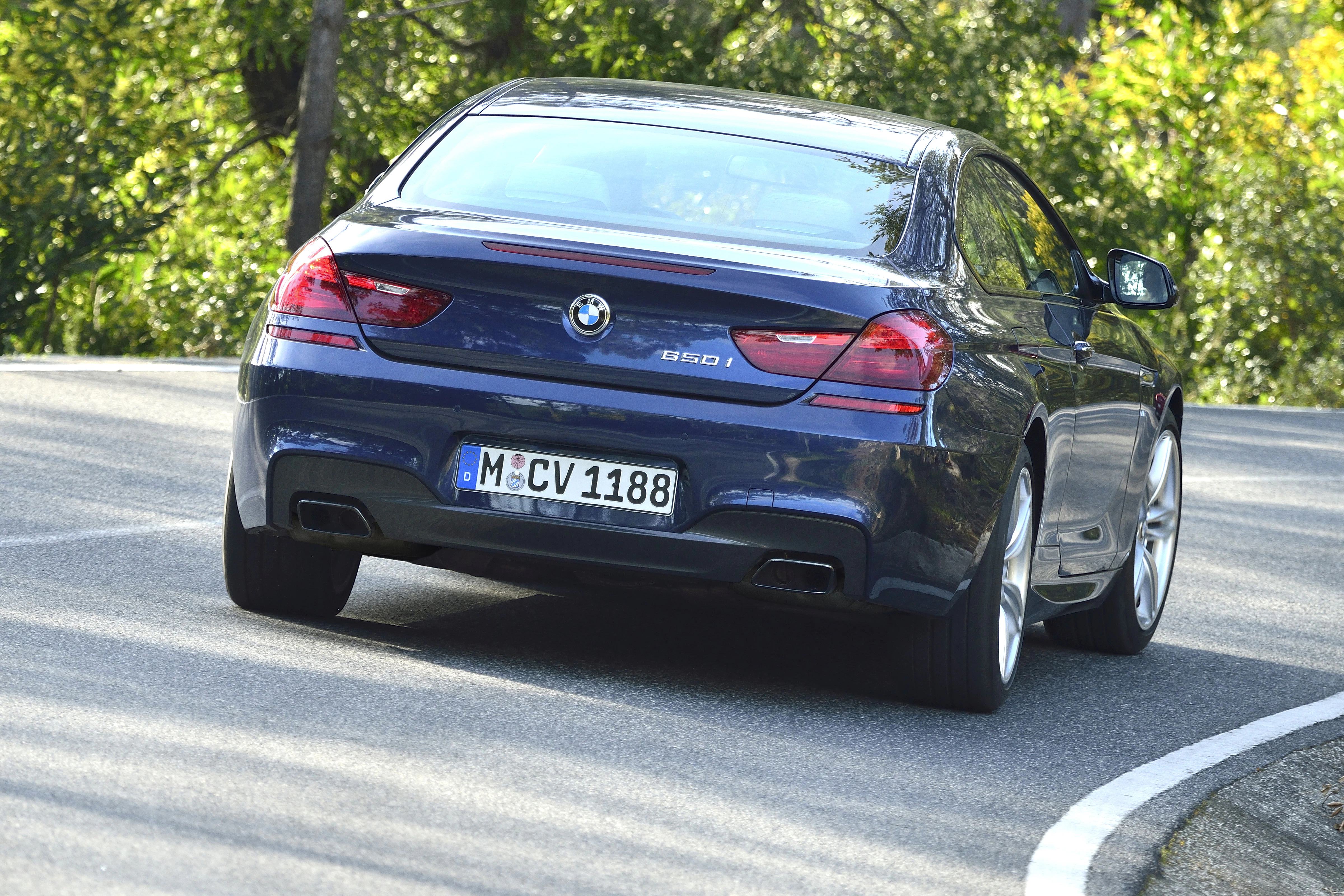 Blauer BMW 650i fährt dynamisch auf einer kurvenreichen Straße, umgeben von grüner Vegetation.