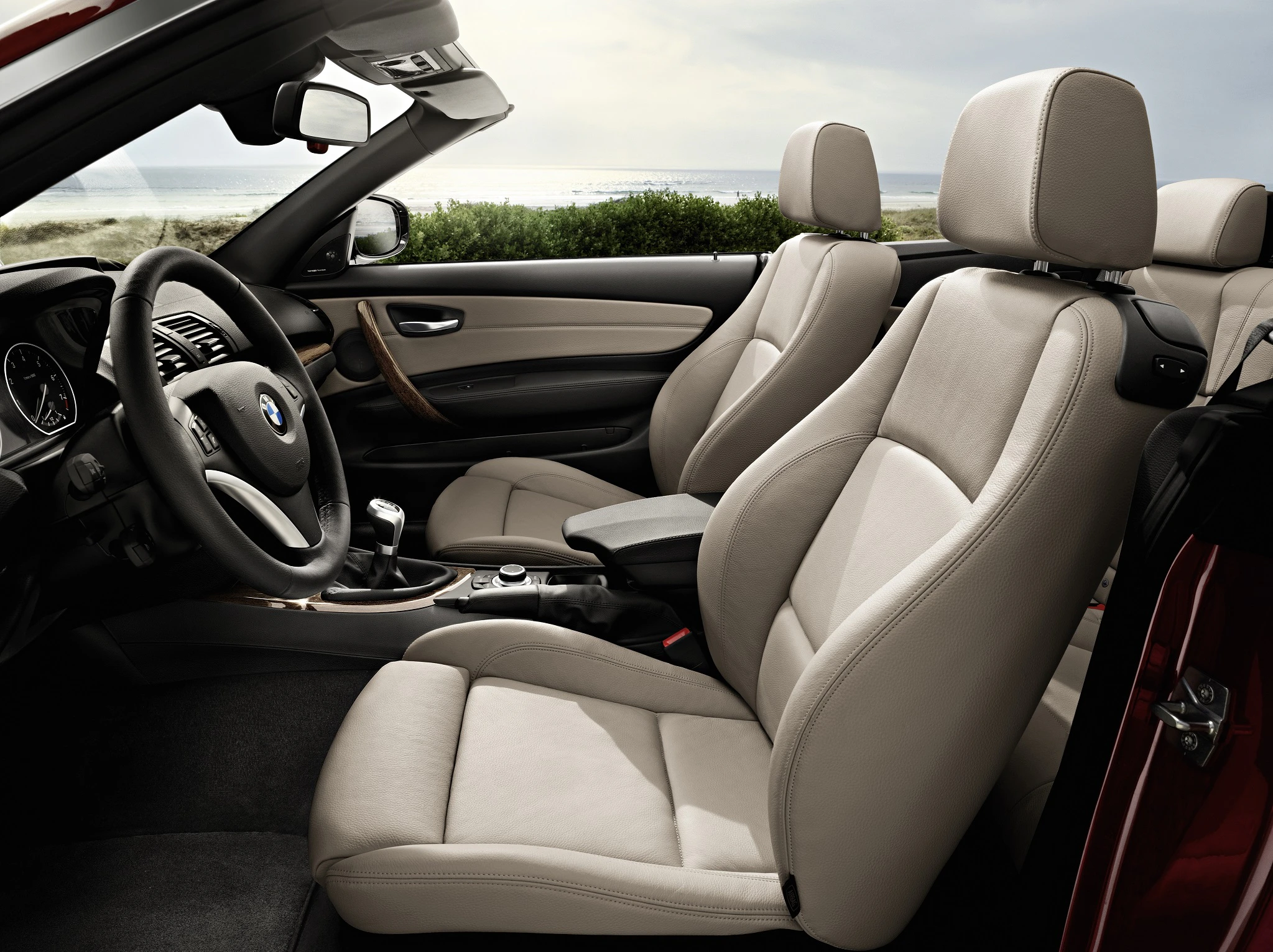 Innenraum eines Cabriolets mit beigen Ledersitzen und modernen Armaturenbrettdesign, mit Blick auf Strandlandschaft im Hintergrund.