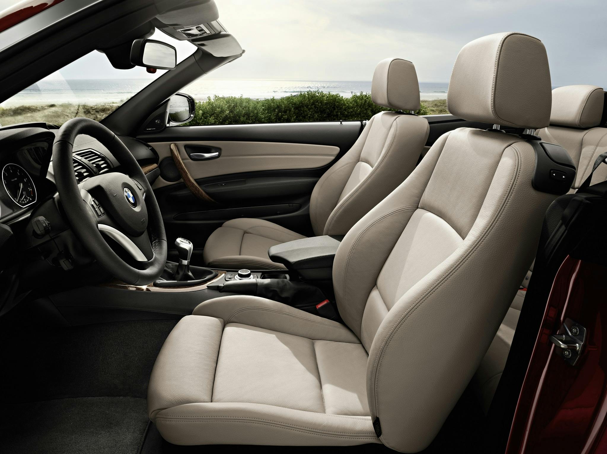 Innenraum eines Cabriolets mit beigen Ledersitzen und modernen Armaturenbrettdesign, mit Blick auf Strandlandschaft im Hintergrund.