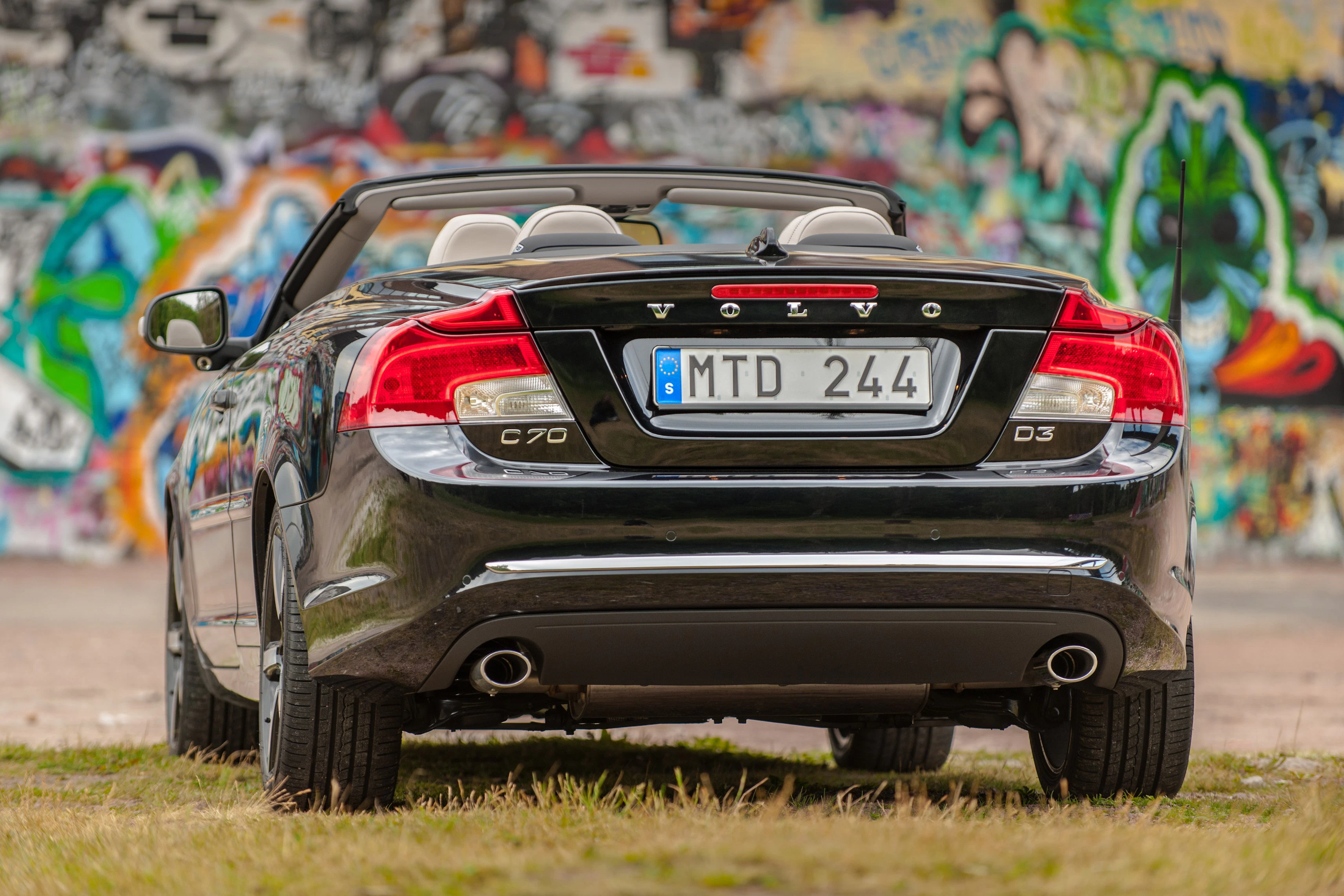 Schwarzer Volvo C70 Cabrio von hinten, auf einer Wiese stehend, vor einer bunten Graffiti-Wand.