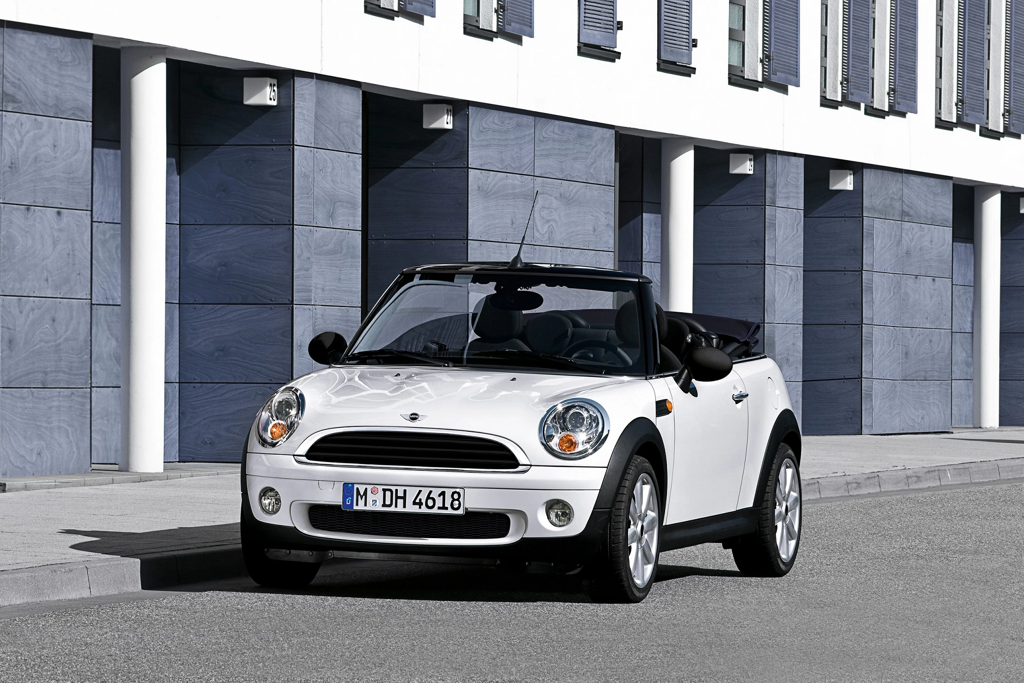 Weißes Cabriolet, geparkt vor einem modernen Gebäude mit blauen Paneelen und weißen Säulen.