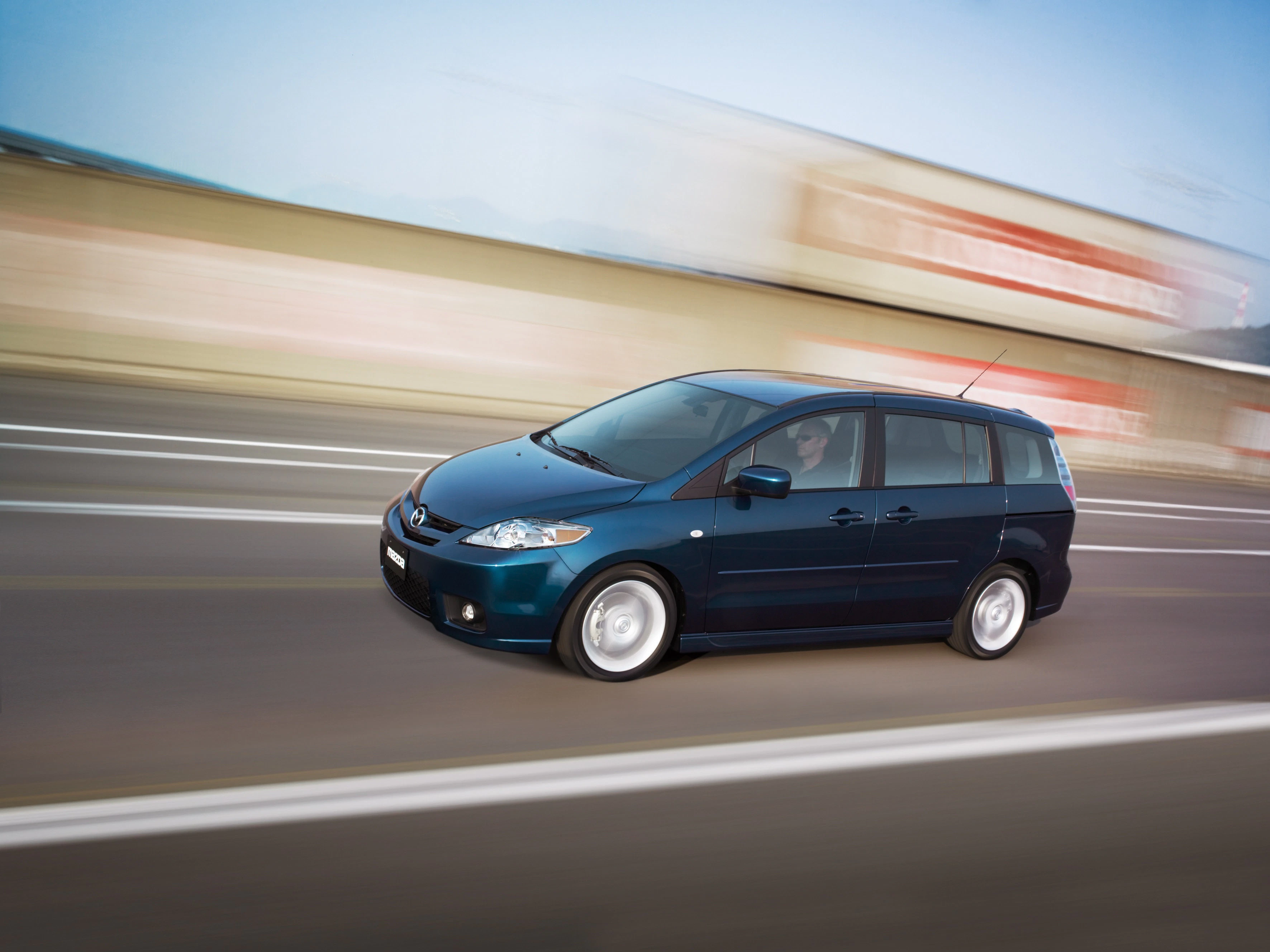 Blauer Minivan fährt schnell auf einer Straße, Hintergrund ist verschwommen, was die Bewegung des Fahrzeugs unterstreicht.