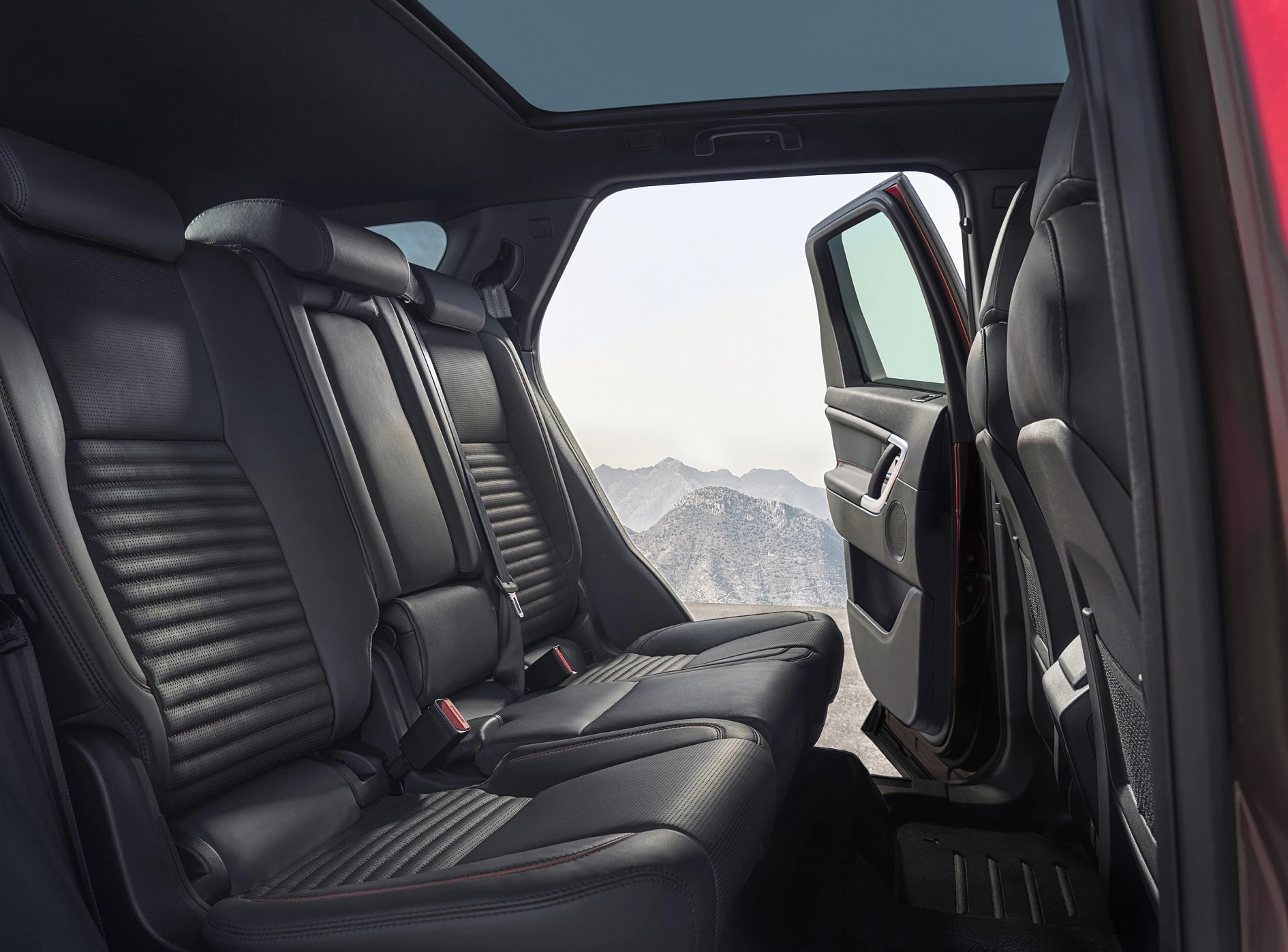 Rückansicht eines Autos mit geöffnetem Tür, schwarzen Ledersitzen und Panoramadach, im Hintergrund Berglandschaft.