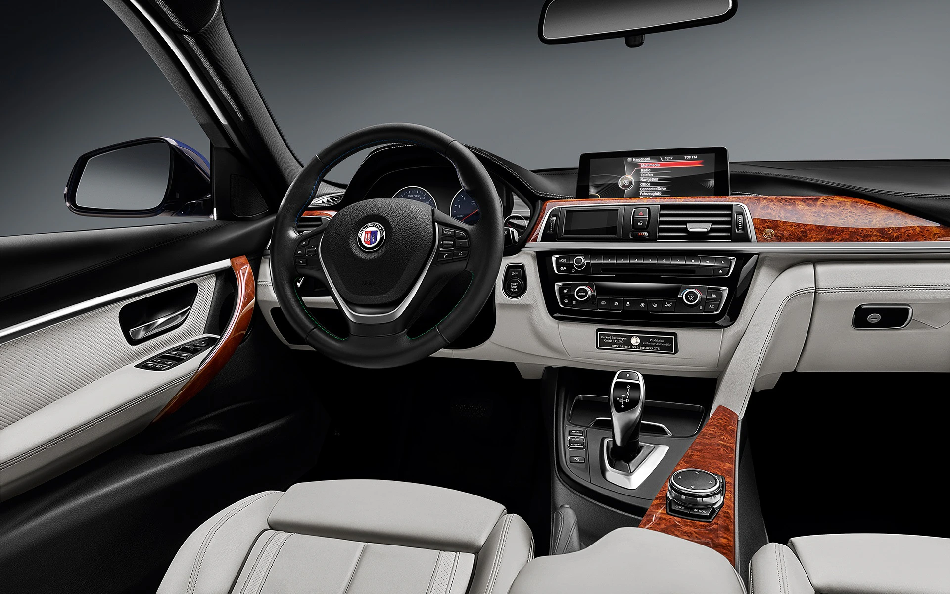 Innenraum eines modernen Autos mit beigen Ledersitzen, schwarzem Lenkrad, Holzverkleidung und einem digitalen Display auf der Mittelkonsole.
