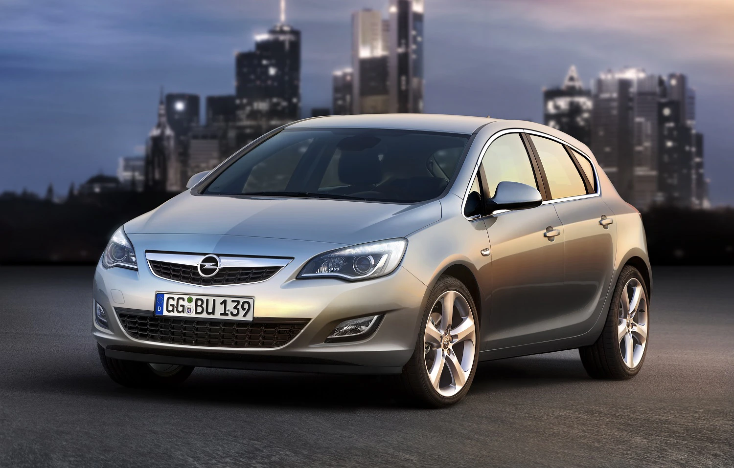 Silberner Opel Astra vor einer urbanen Skyline in der Dämmerung, fahrbereit und dynamisch präsentiert.