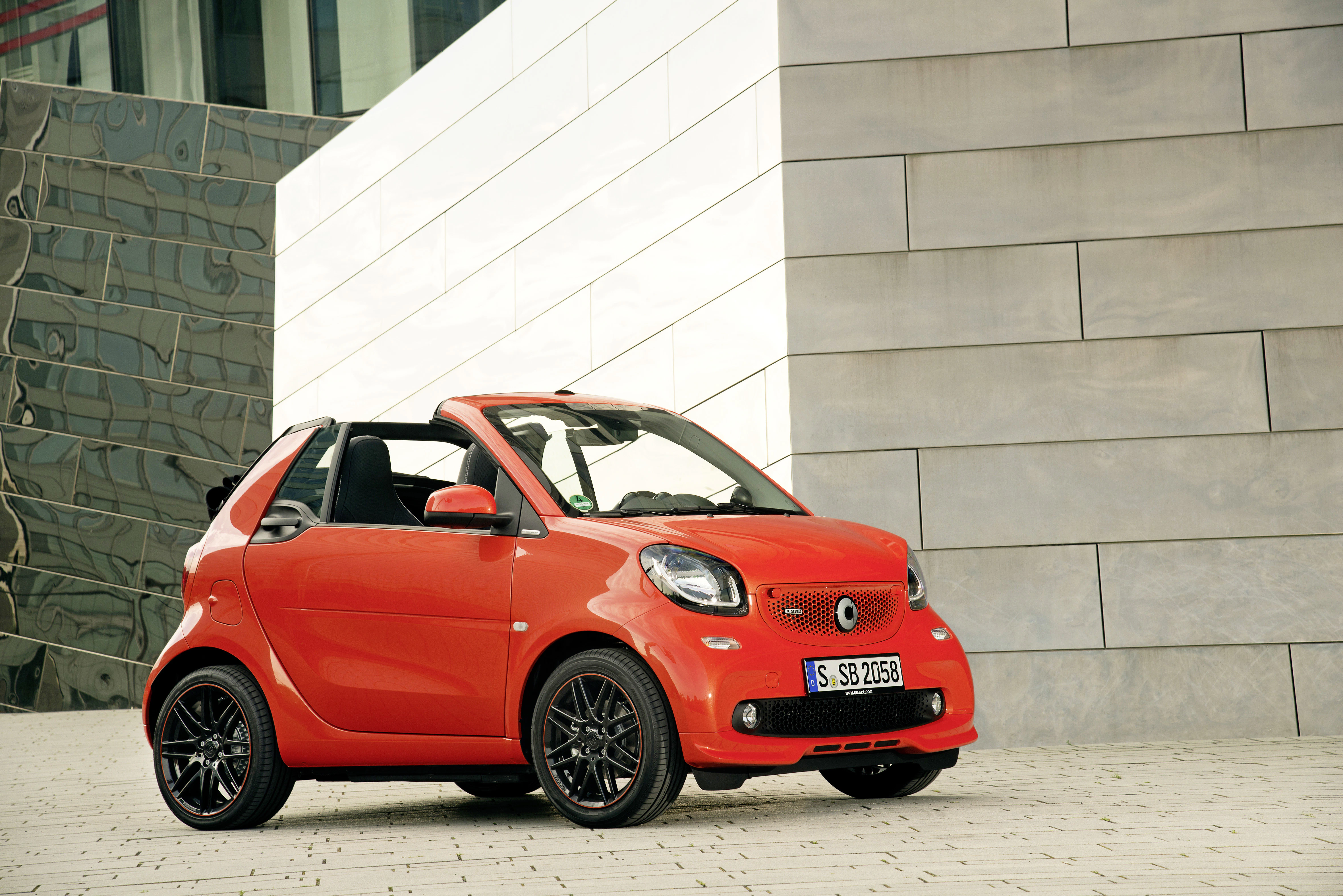 Roter Smart Cabrio parkt auf einem modernen, urbanen Hintergrund mit Architektur aus Glas und Stein.