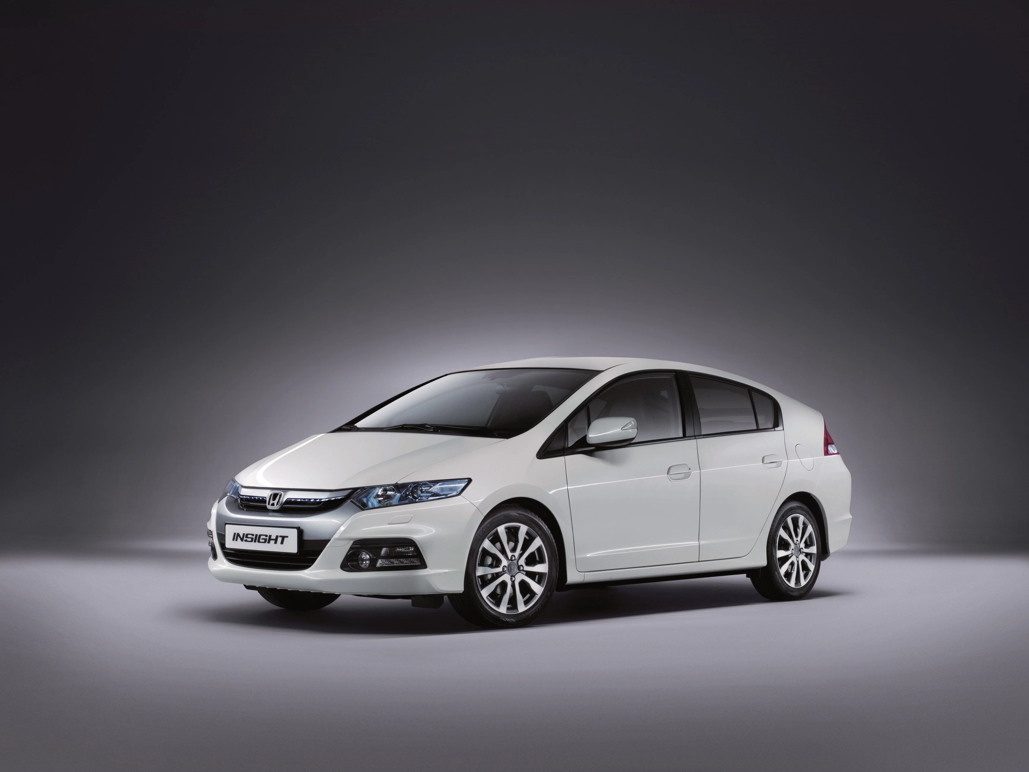 Weißer Honda Insight Hybridauto, seitlich vor grauem Hintergrund präsentiert, mit markanten Scheinwerfern und glänzenden Felgen.