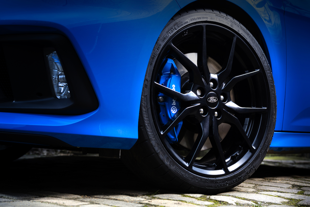 Nahaufnahme eines blauen Autos mit stilvollem schwarzen Leichtmetallrad und blauer Bremse auf gepflasterter Straße.