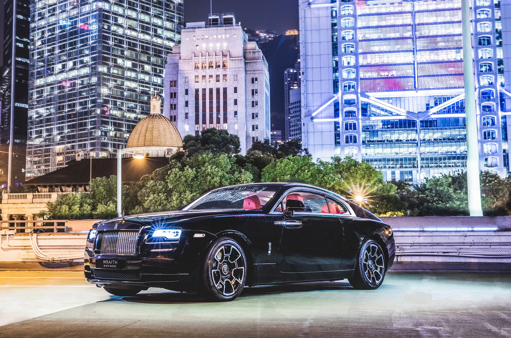 Luxuriöses schwarzes Auto, nachts vor beleuchteten Wolkenkratzern in einer Stadtlandschaft geparkt.