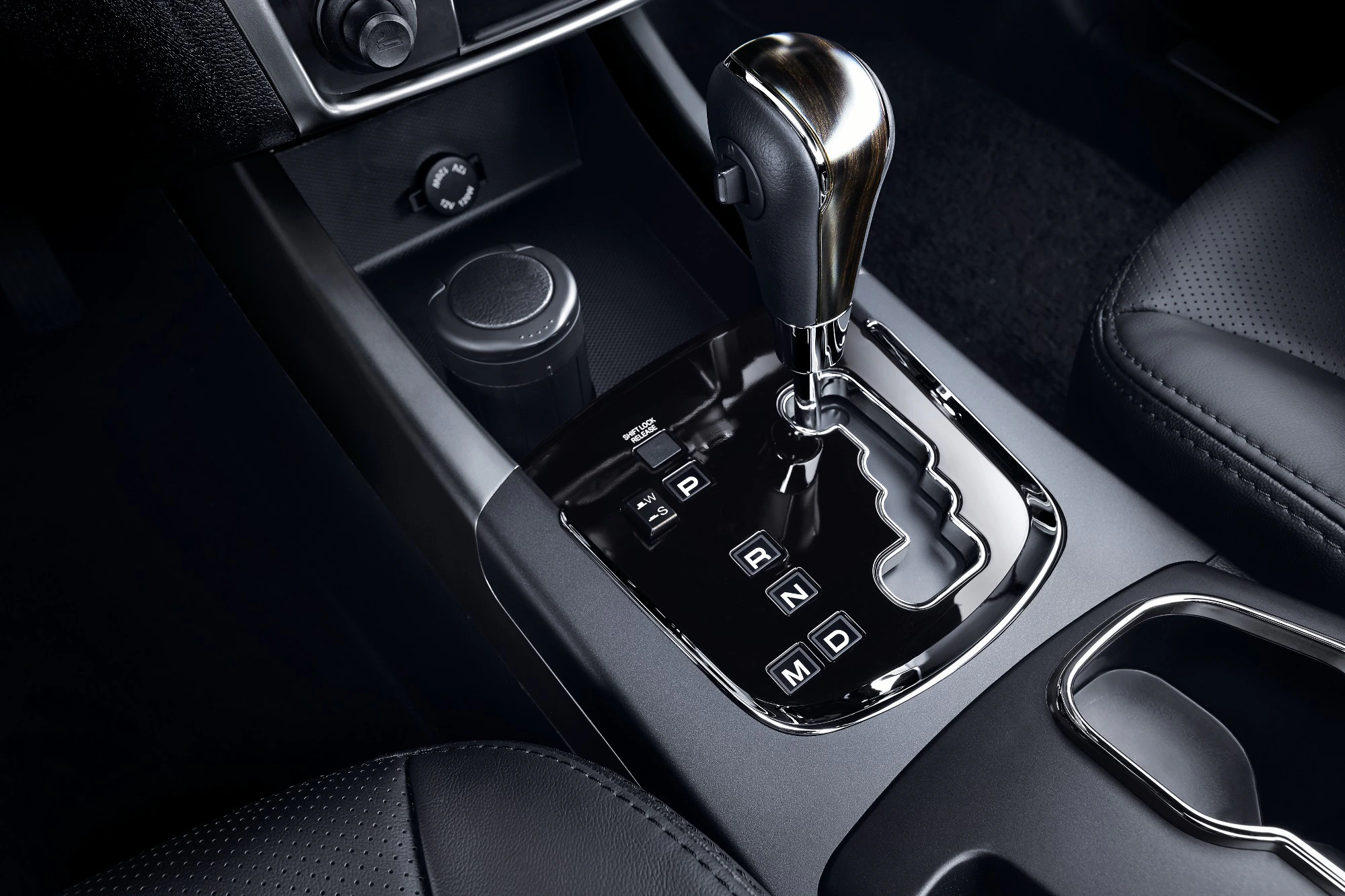 Nahaufnahme eines Automatikgetriebes in einem Auto, mit sichtbaren Gangpositionen und glänzendem Schalthebel.