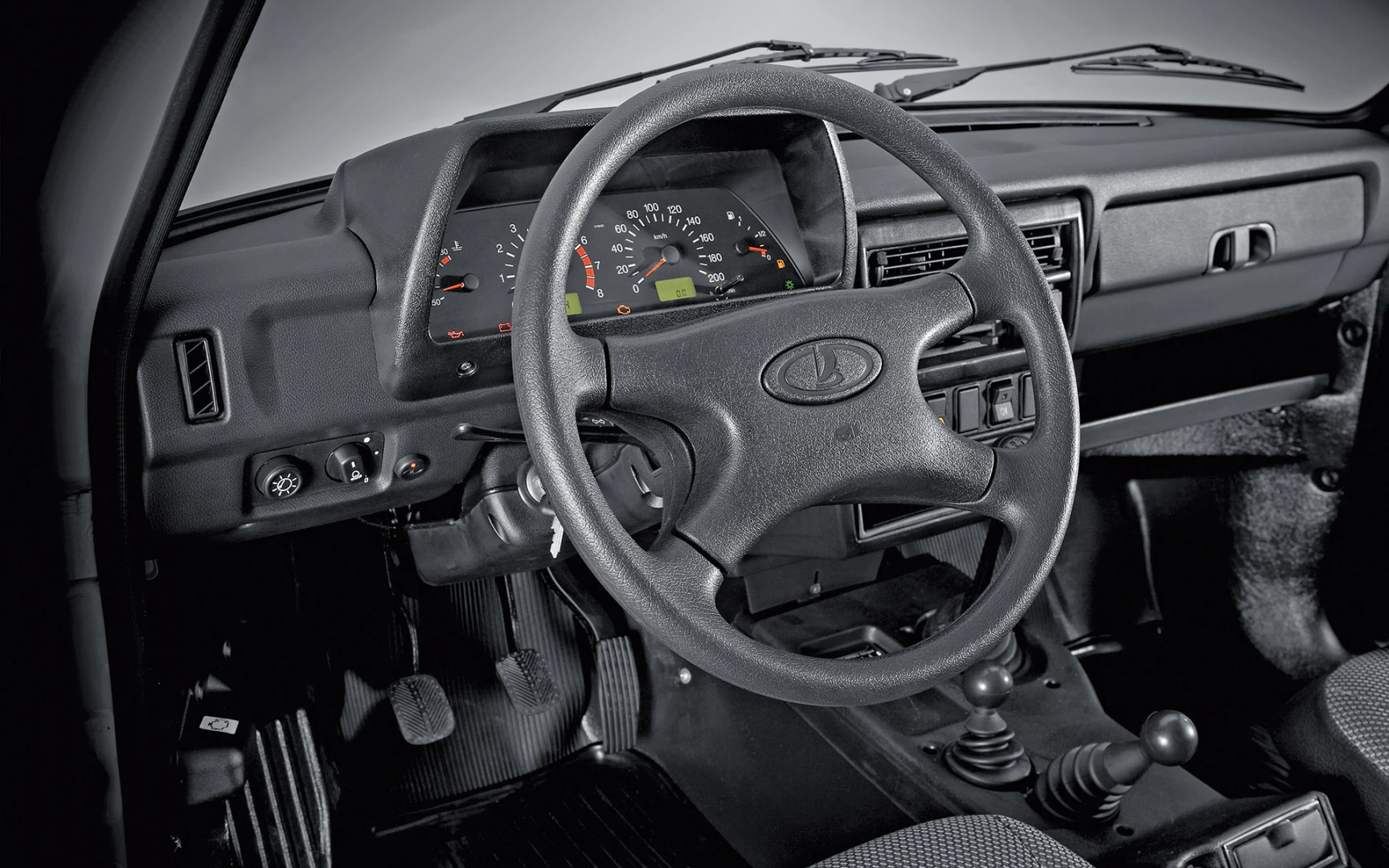 Innenraum eines Fahrzeugs mit schwarzem Lenkrad, Armaturenbrett und Schalthebel. Klassisches Design mit analogen Anzeigen.
