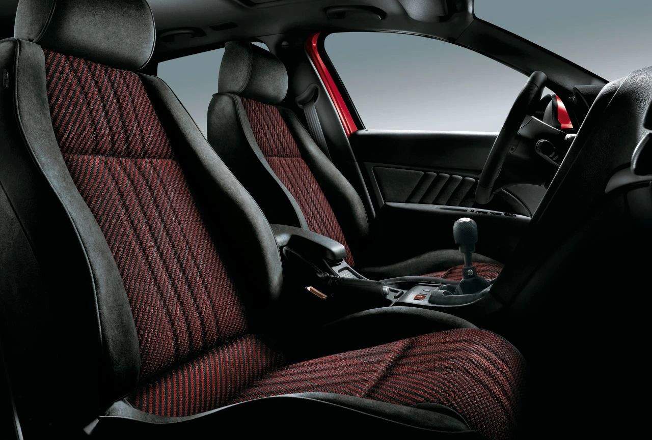 Die Innenraumansicht eines Autos zeigt schwarze und rot gemusterte Sitze mit einem Handschaltgetriebe.