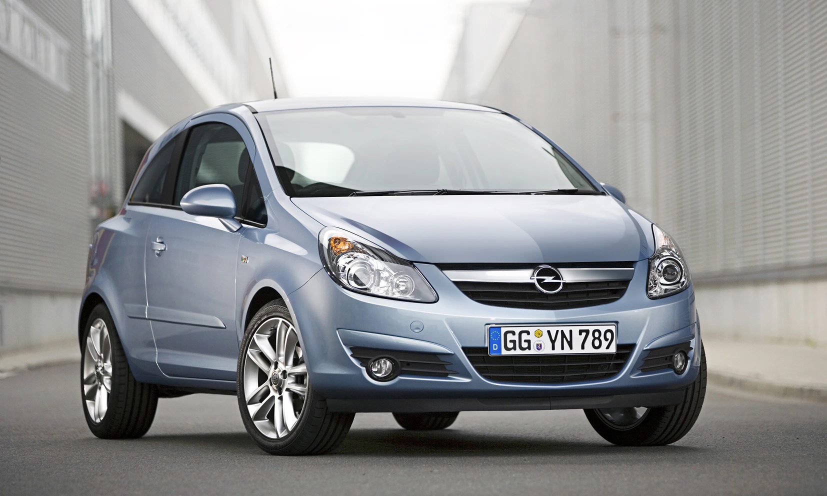 Silberner Opel Corsa, Vorderansicht, auf einer Straße zwischen zwei Gebäuden geparkt. Fahrzeug hat ein deutsches Nummernschild.