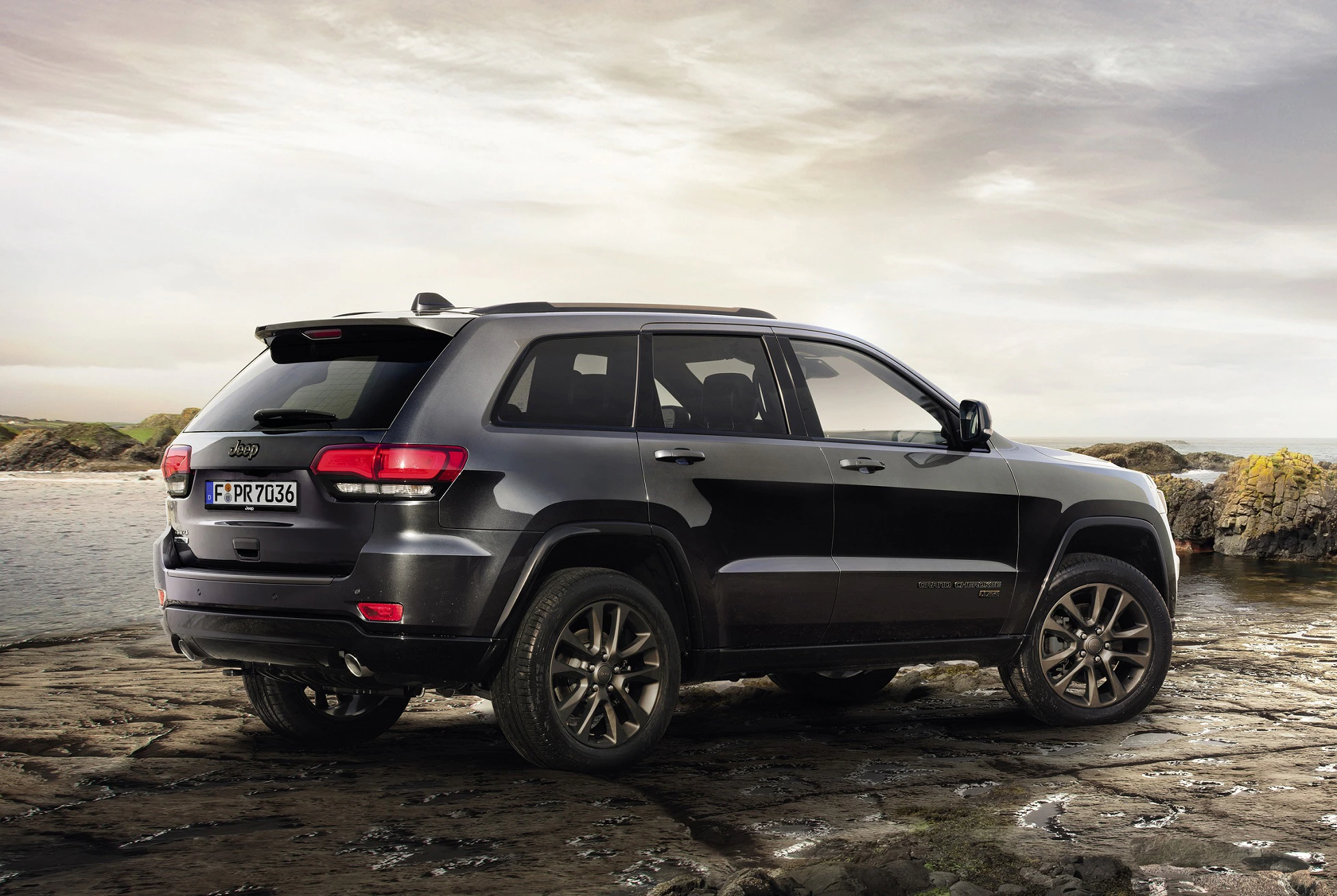 Ein schwarzer SUV steht auf einem felsigen Untergrund vor einer Küstenlandschaft mit bewölktem Himmel im Hintergrund.
