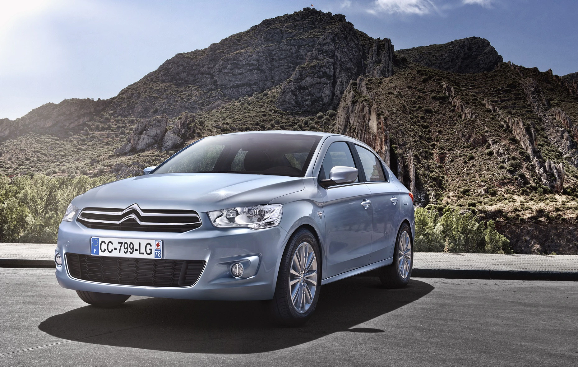 Silberner Citroën C-Elysée steht auf einer Straße vor einer Berglandschaft unter blauem Himmel.