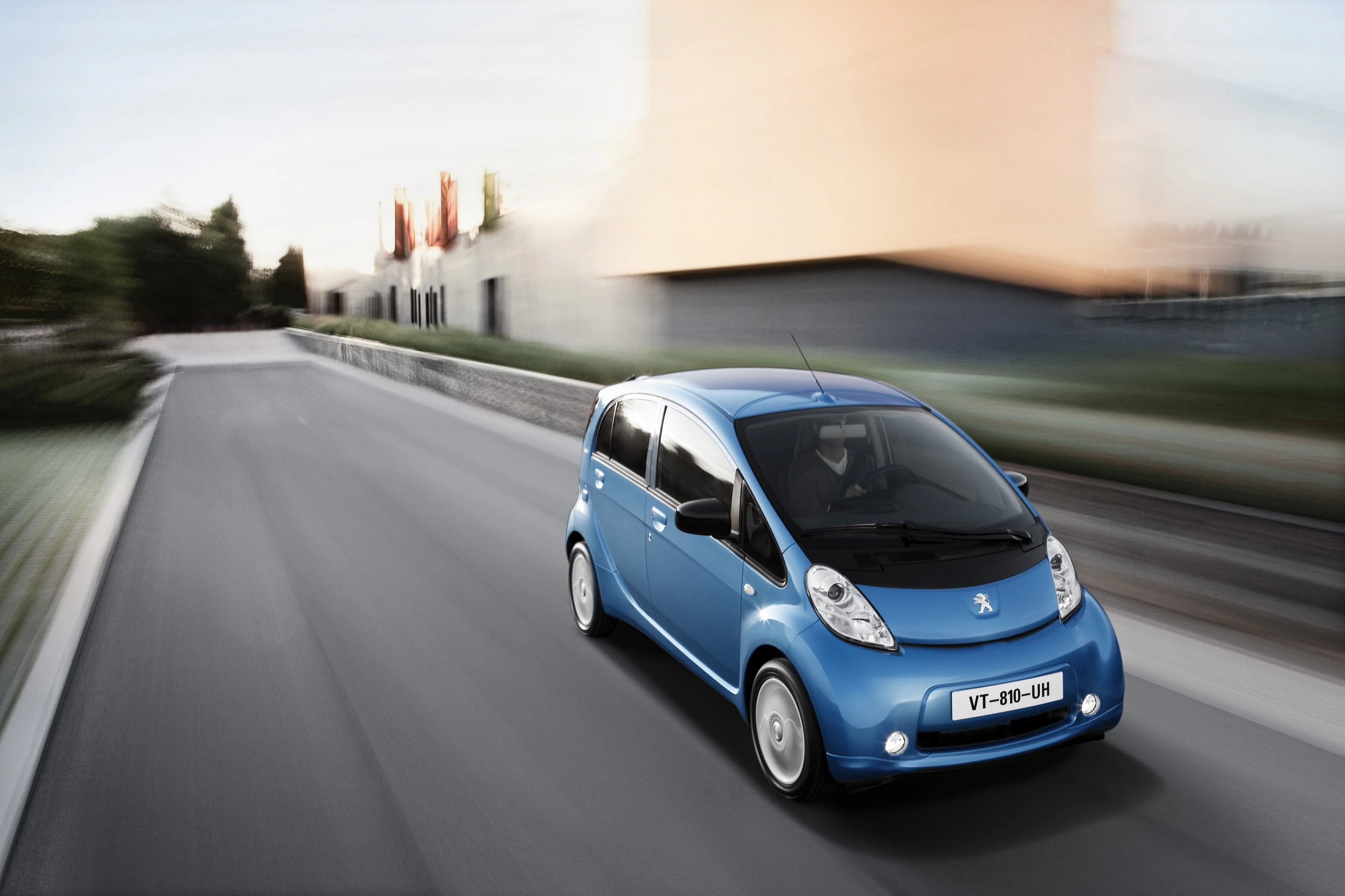 Blaues Elektroauto fährt schnell auf einer städtischen Straße, moderne Gebäude im Hintergrund.