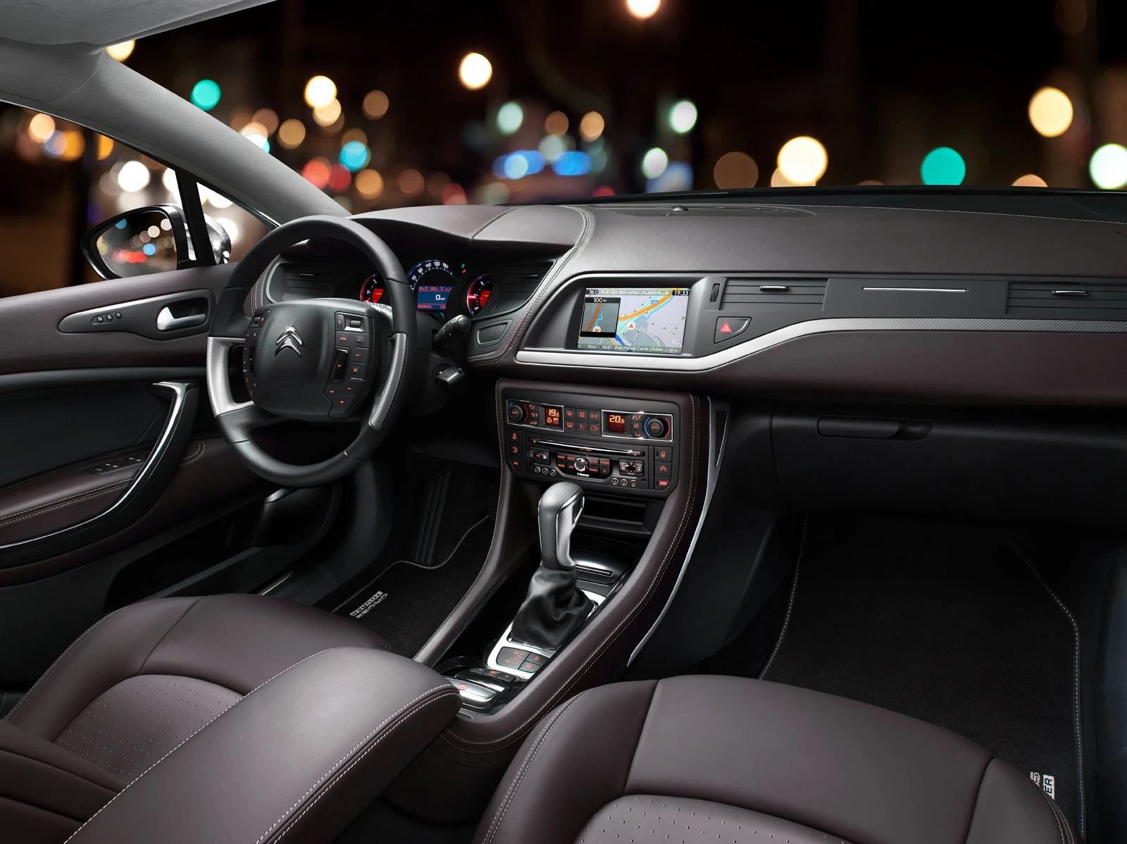 Innenraum eines Autos bei Nacht, mit moderner Armaturentafel, Navigationssystem auf dem Bildschirm und eleganten, braunen Ledersitzen.