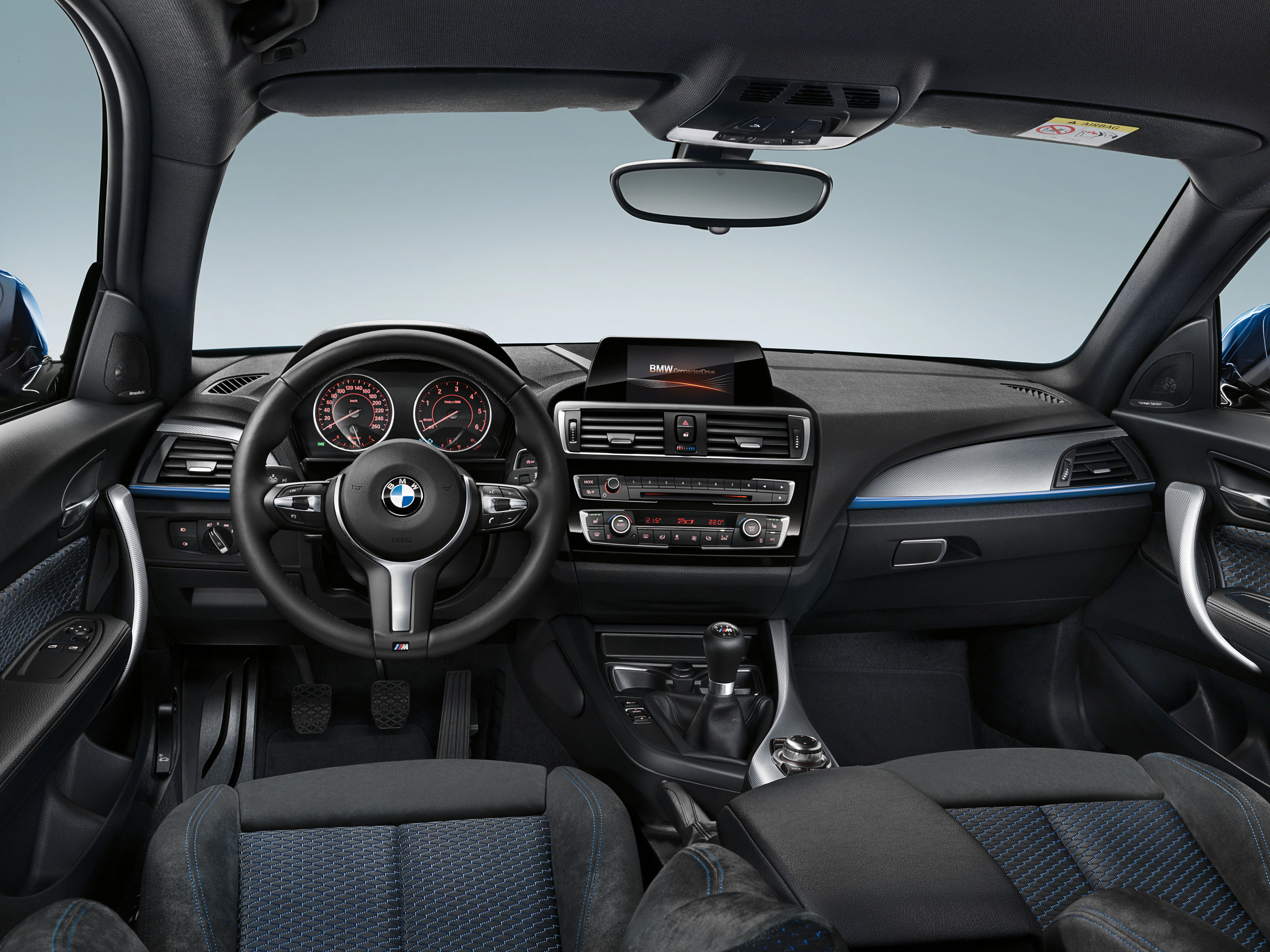 Innenraum eines BMWs mit Lederlenkrad, Armaturenbrett mit Display, Klimasteuerung und Schalthebel, moderne Ausstattung in Schwarz und Blau.