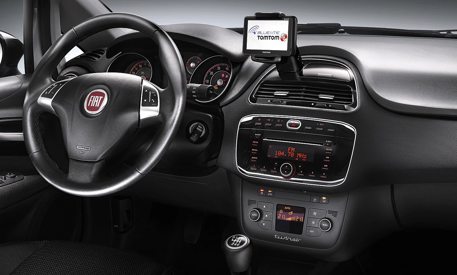 Innenansicht eines Fiat-Autos mit Armaturenbrett, Lenkrad, eingebautem Radio und einem TomTom-Navigationsgerät auf dem Armaturenbrett.