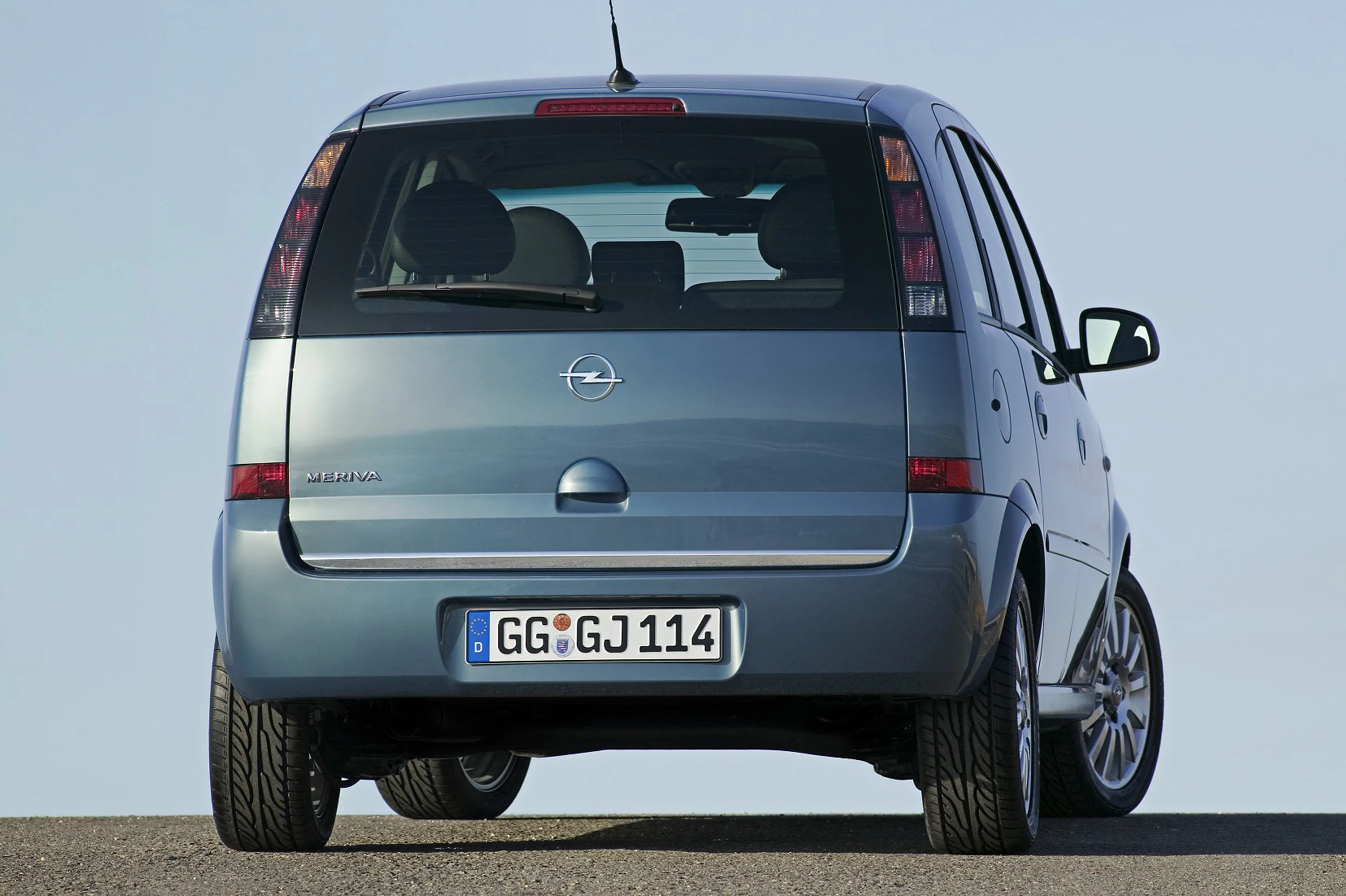 Rückansicht eines blauen Opel Meriva mit deutschem Kennzeichen auf einer Straße vor blauem Himmel.