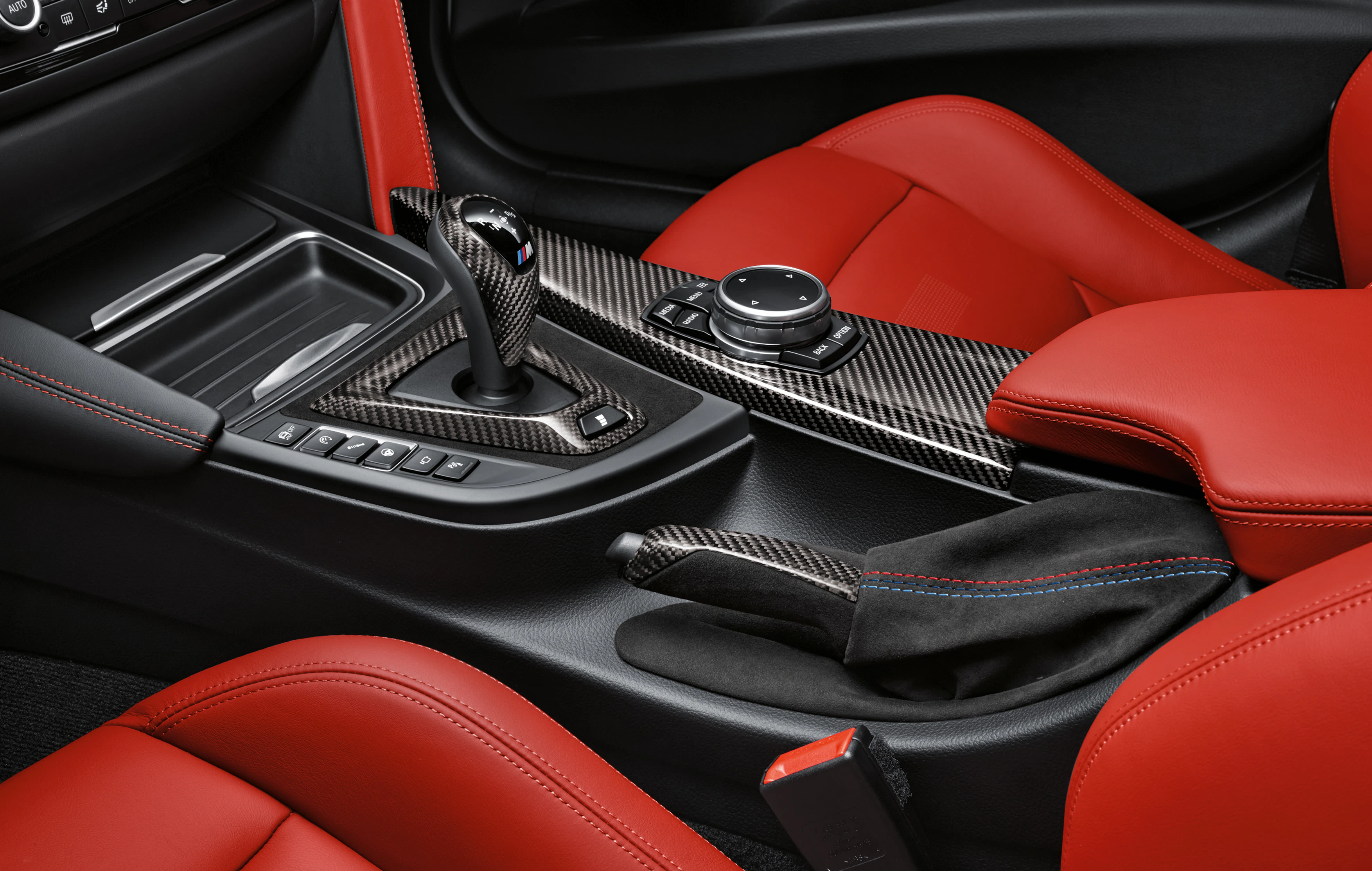Nahaufnahme des Innenraums eines Autos mit roten Ledersitzen, einem Schalthebel und einem zentralen Bedienknopf auf der Mittelkonsole.