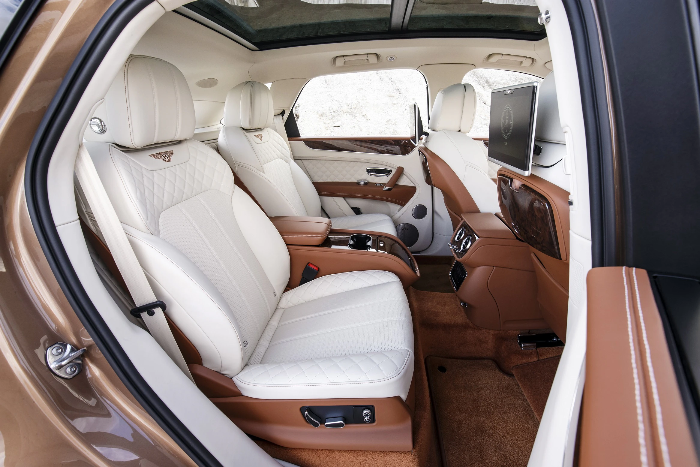 Luxuriöser Autoinnenraum mit weißen Ledersitzen, Panoramadach, Bildschirmen und eleganten Holzakzenten in Beige- und Brauntönen.