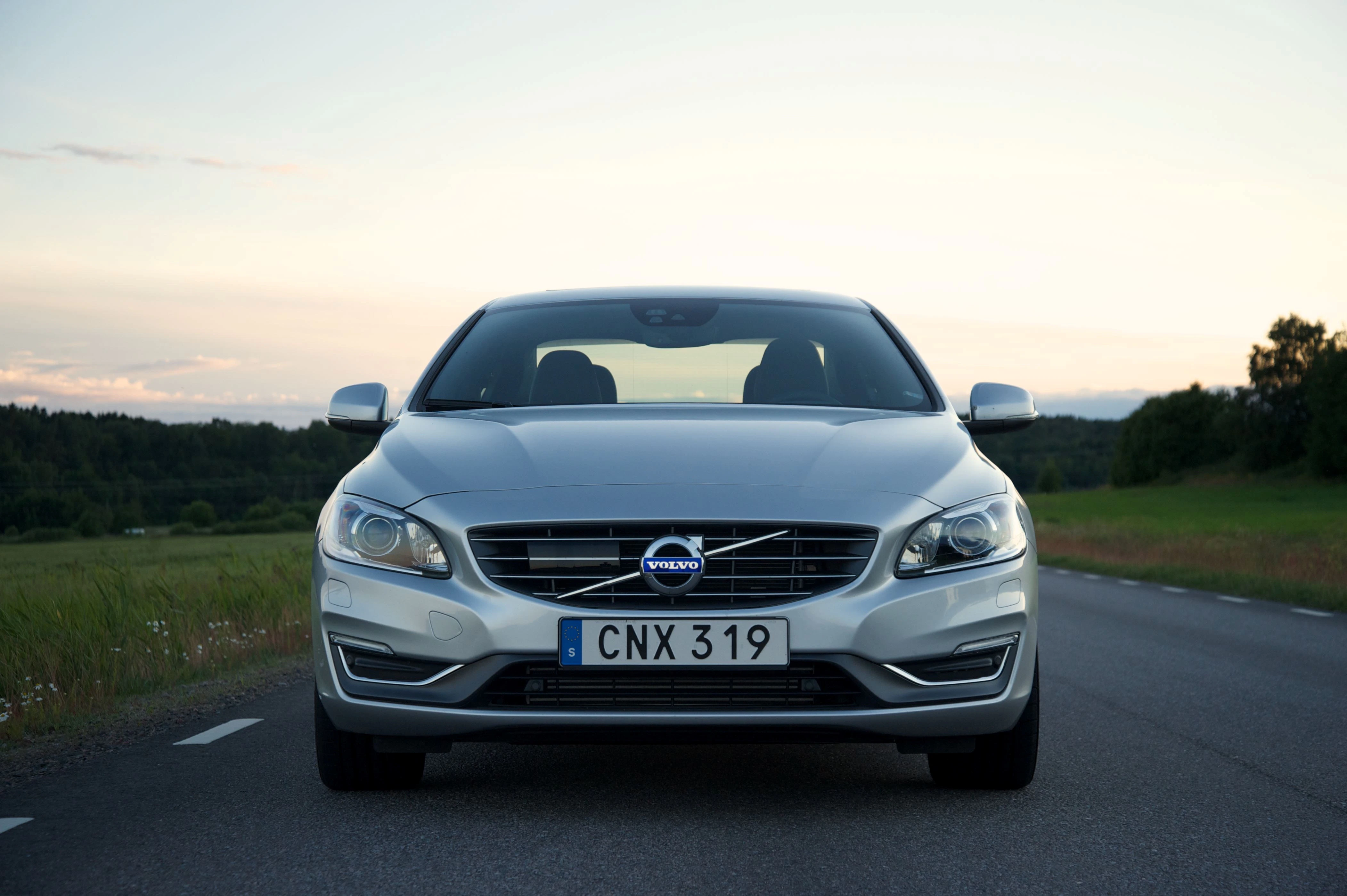 Silberner Volvo auf einer Landstraße bei Sonnenuntergang, frontal fotografiert, mit Bäumen im Hintergrund. Nummernschild: CNX 319.