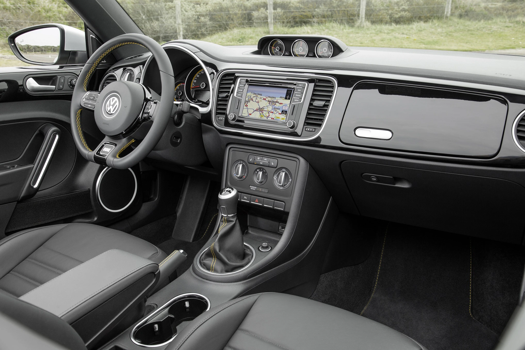 Innenraum eines VW-Autos mit Lenkrad, Navigationssystem, Schalthebel und Armaturenbrett. Elegante schwarze Lederausstattung.