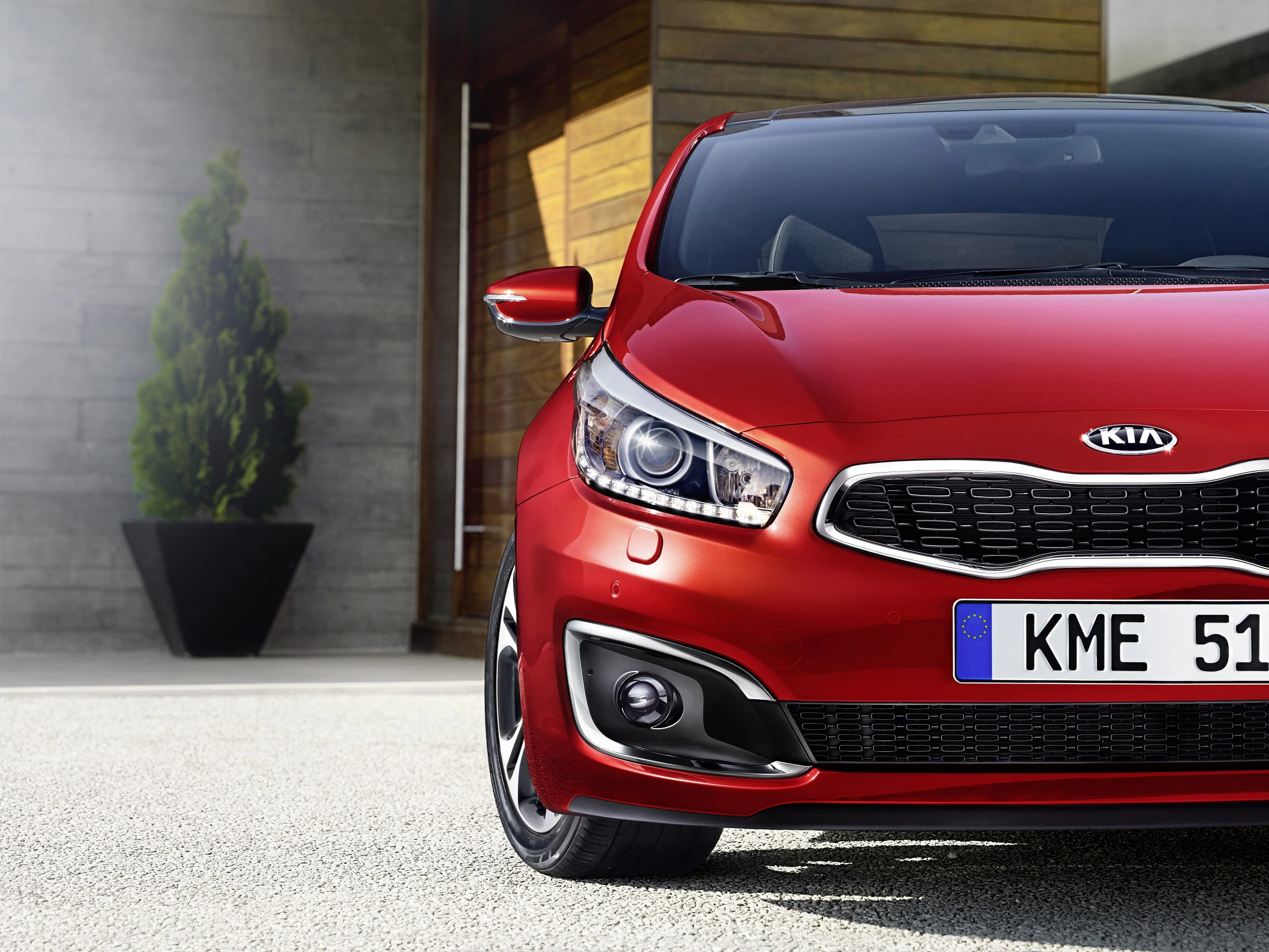 Roter Kia Ceed vor modernem Gebäude, schräg von vorne fotografiert. Europäisches Nummernschild, rechter Scheinwerfer und ein Pflanzenkübel im Hintergrund.