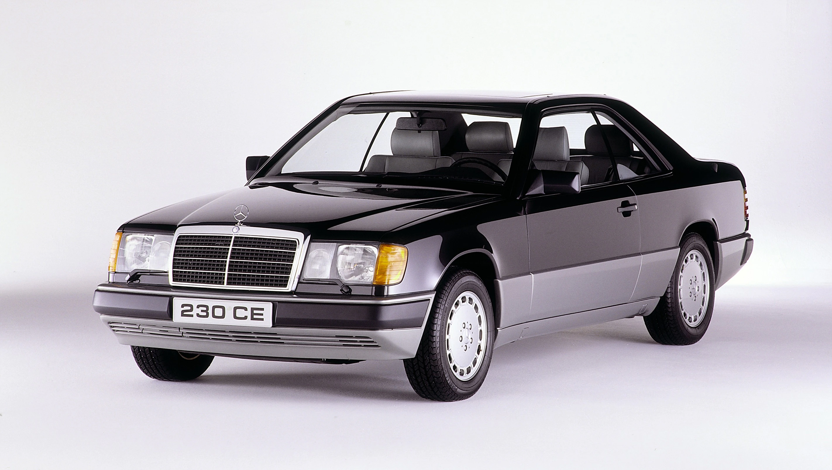 Schwarzer Mercedes-Benz 230 CE Coupé, Baujahr um 1990, mit silbernen Akzenten, fotografiert vor weißem Hintergrund.