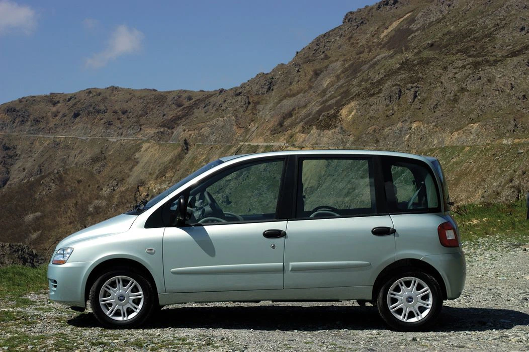 Silberner Minivan steht auf einer Schotterstraße vor einer felsigen Berglandschaft unter klarem Himmel.