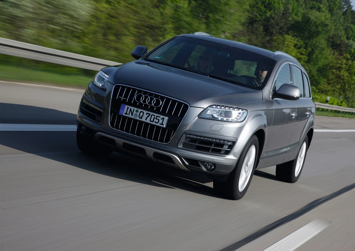 Silberner Audi Q7 fährt schnell auf einer Autobahn mit verschwommenem Hintergrund aus grünen Bäumen.