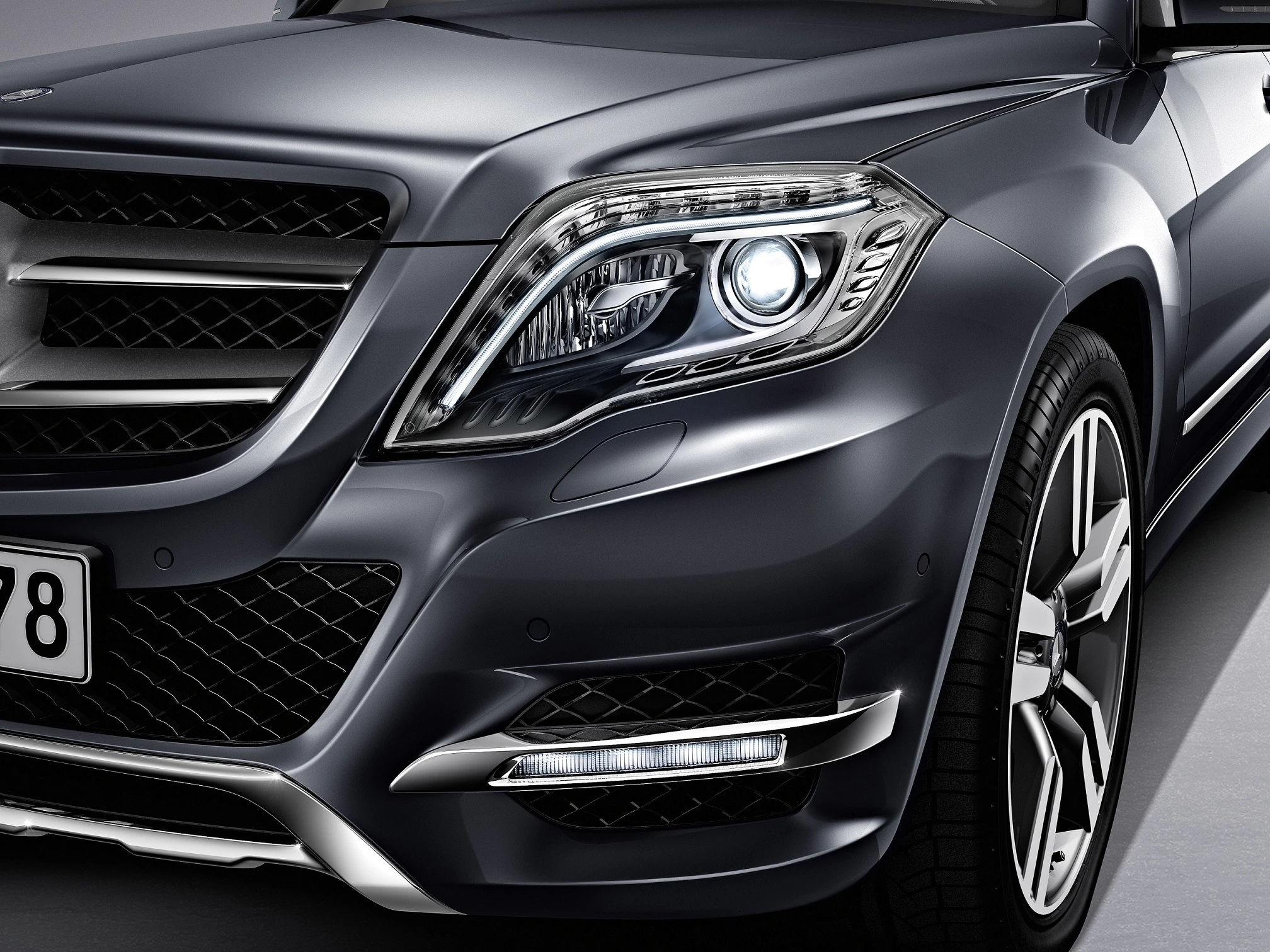 Nahaufnahme eines modernen SUV-Frontbereichs in dunklem Metallic-Grau mit elegantem, markantem Scheinwerferdesign und glänzendem Kühlergrill.