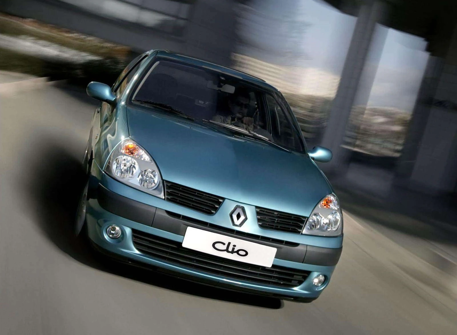 Blauer Renault Clio fährt dynamisch auf einer Straße, umgeben von unscharfem Hintergrund, was Bewegung betont.